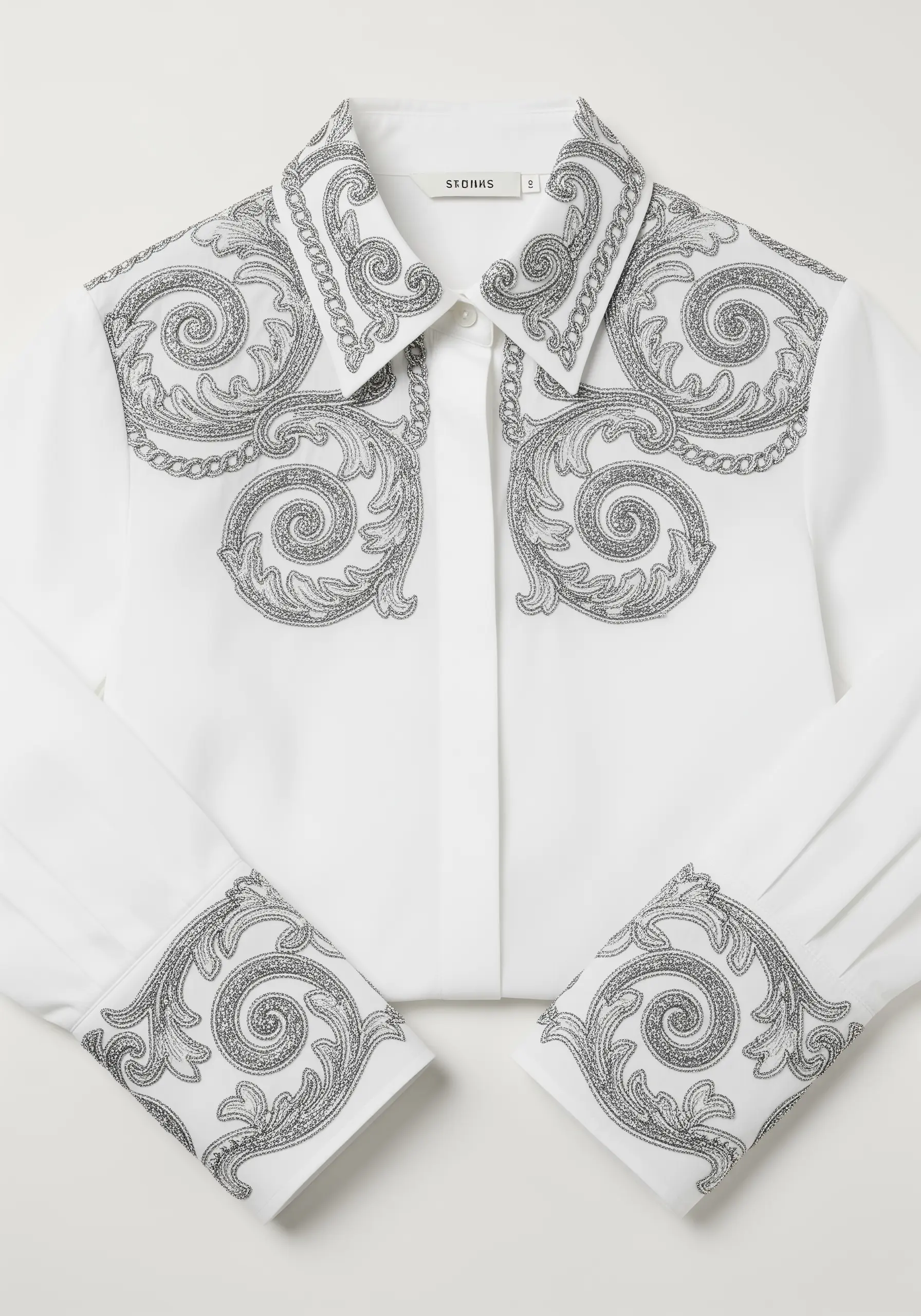 Intricate silver glitter scrollwork embroidery on the collar and cuffs of a white shirt.