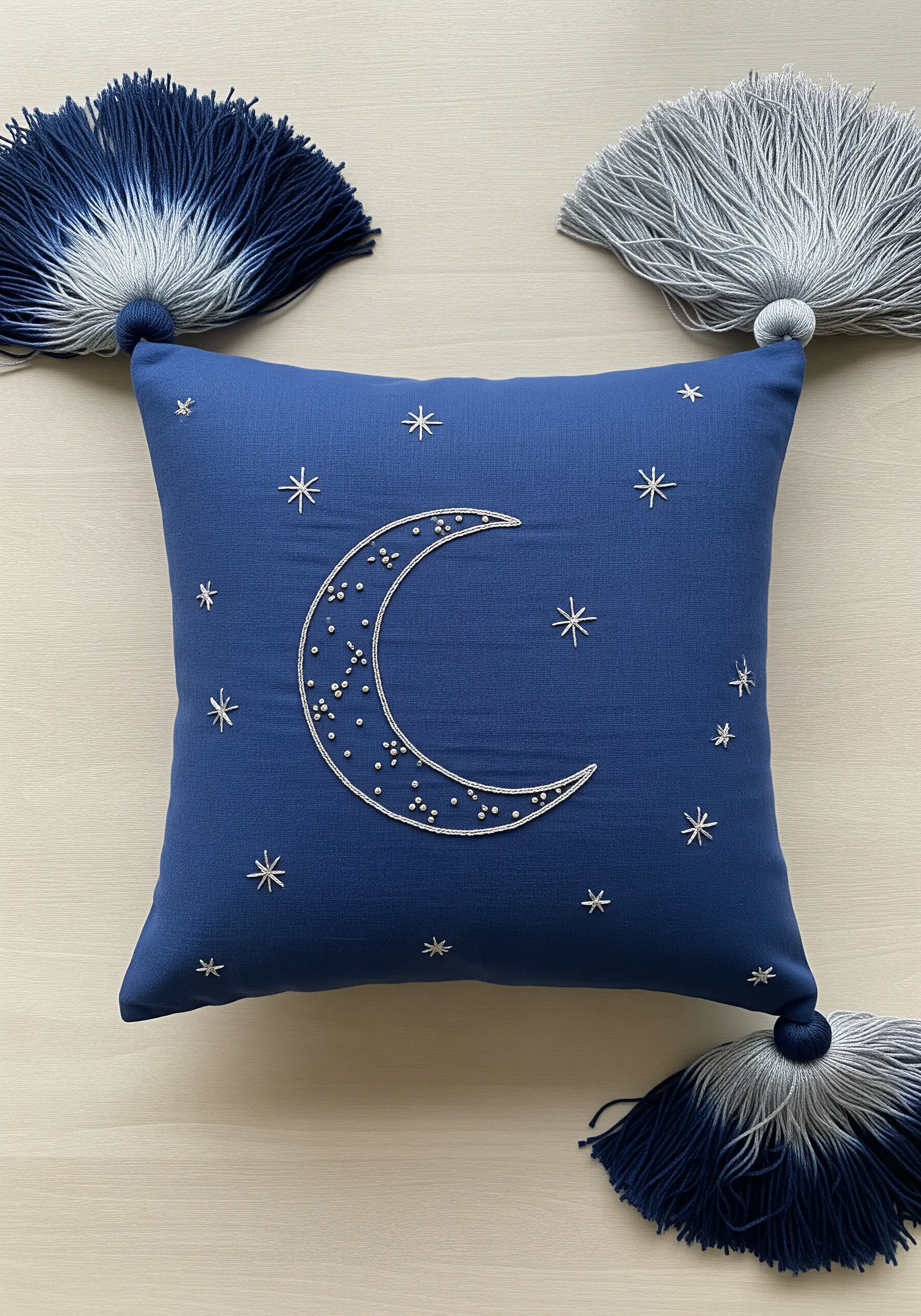Embroidered crescent moon filled with beads on a blue pillow with ombre tassels.