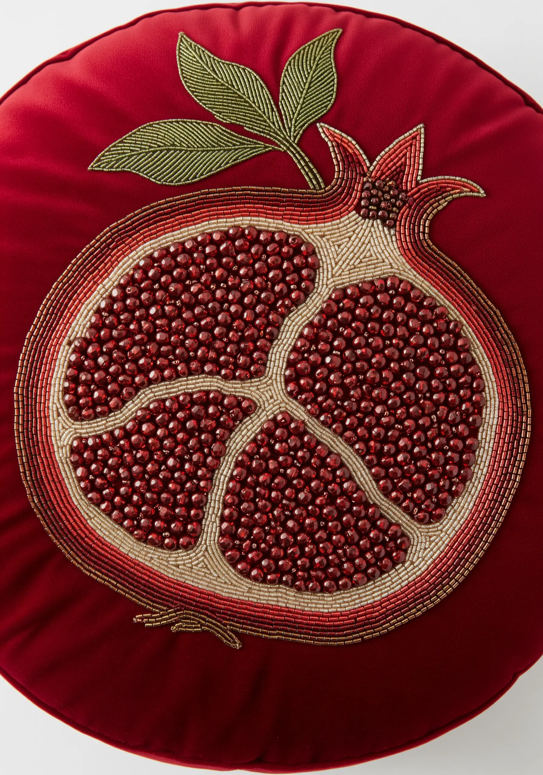 A beaded pomegranate motif on a round red cushion, with seeds made of red beads.