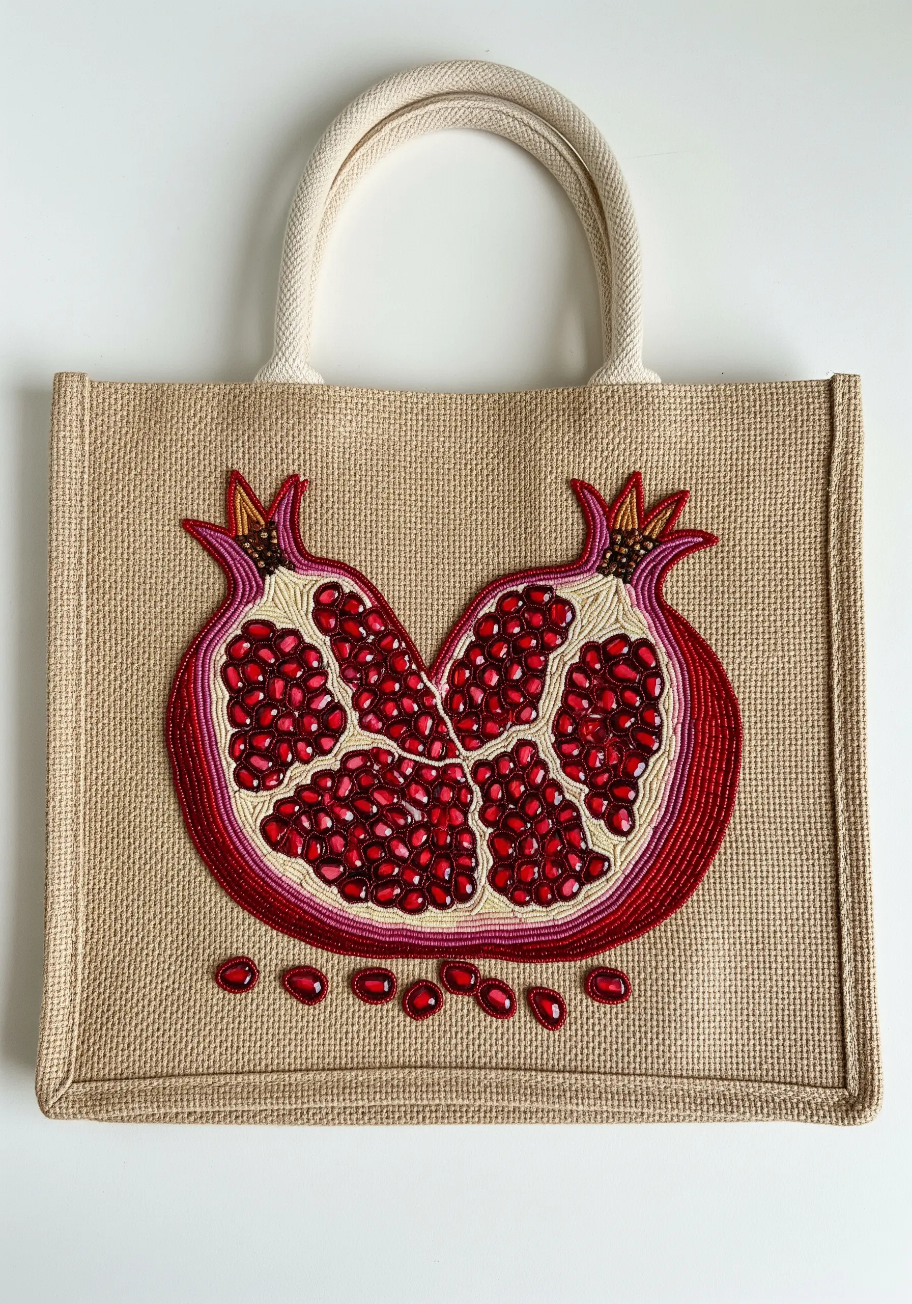A heart-shaped pomegranate embroidered and beaded onto a rustic burlap tote bag.