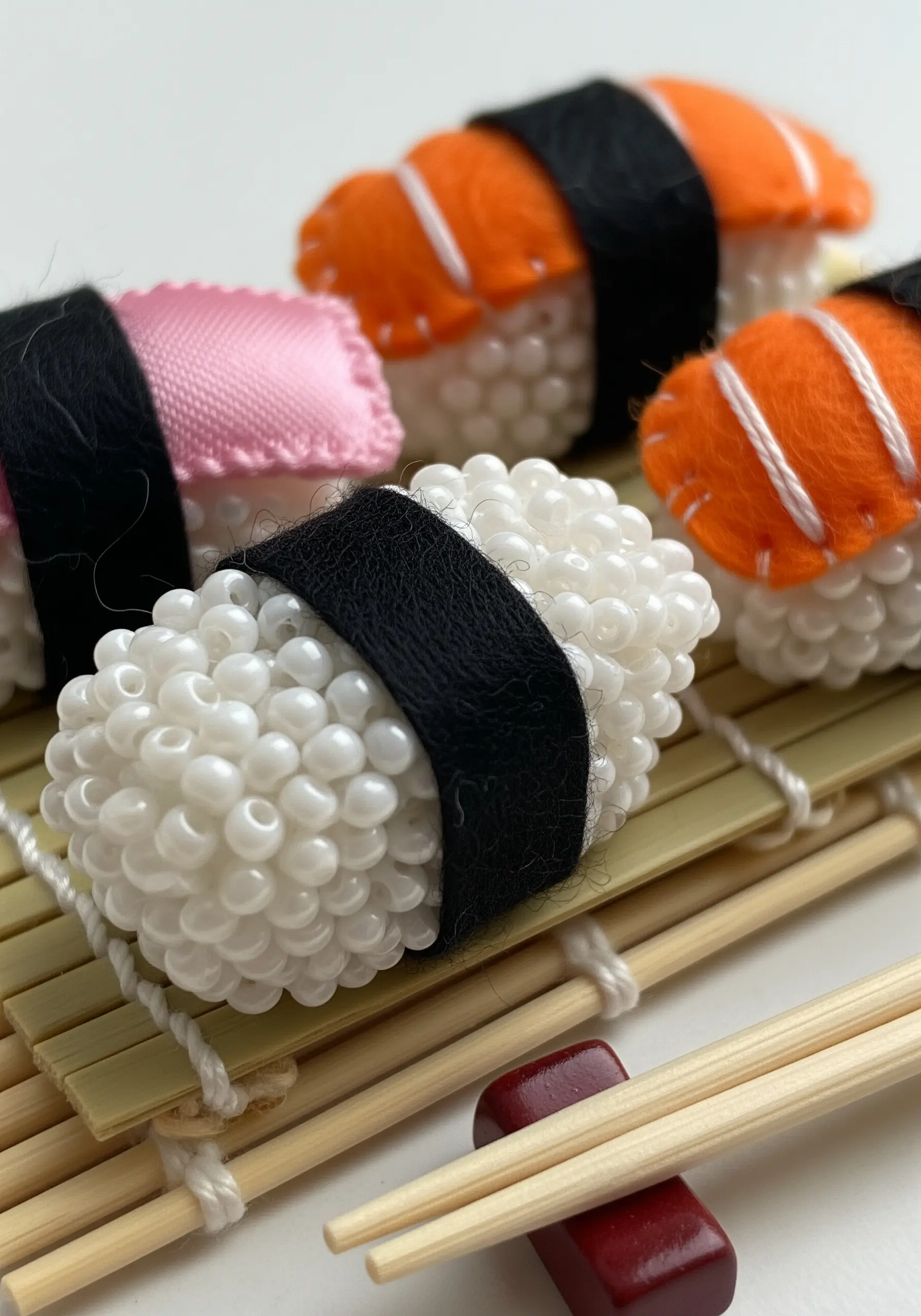 Miniature sushi made from felt and fabric, using tiny white beads for the rice.