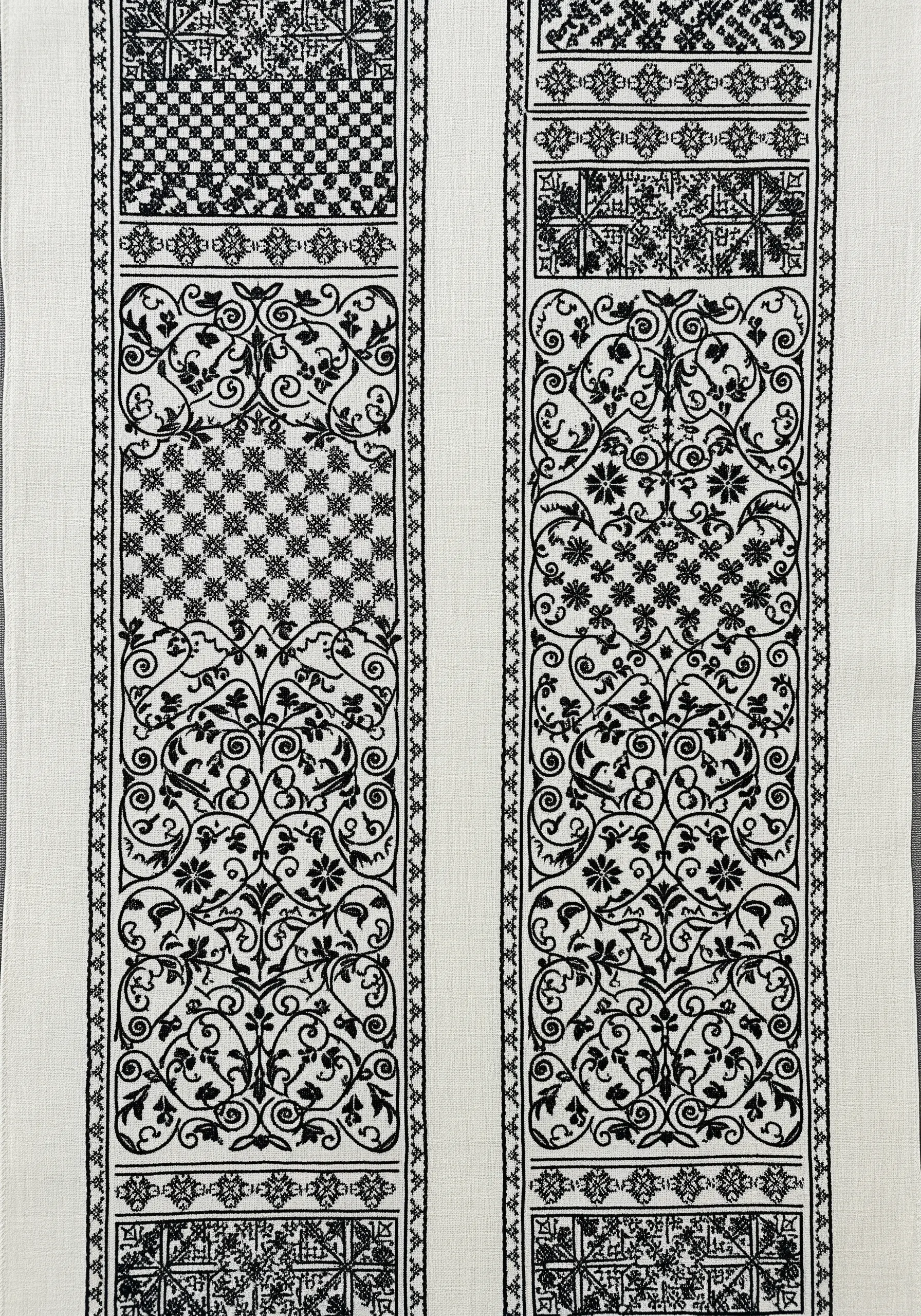 A table runner with vertical panels of intricate, blackwork-style geometric and floral patterns.