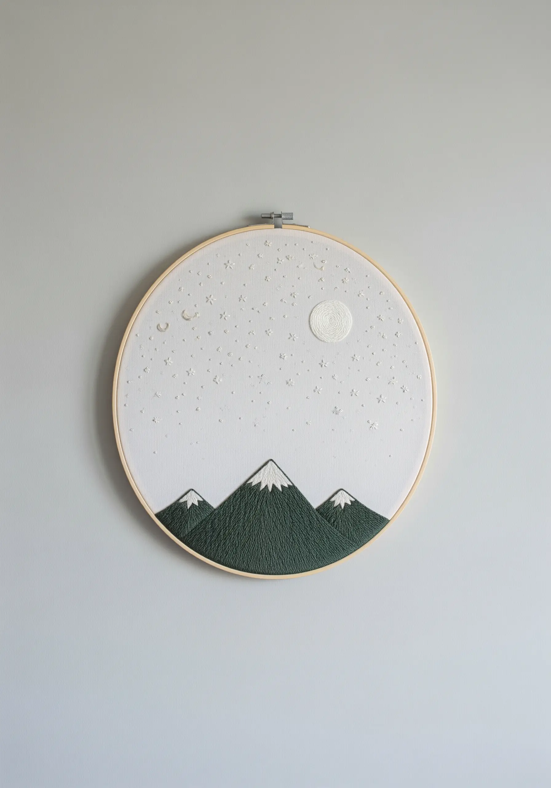 Minimalist embroidery of mountains under a starry sky in a wooden hoop.