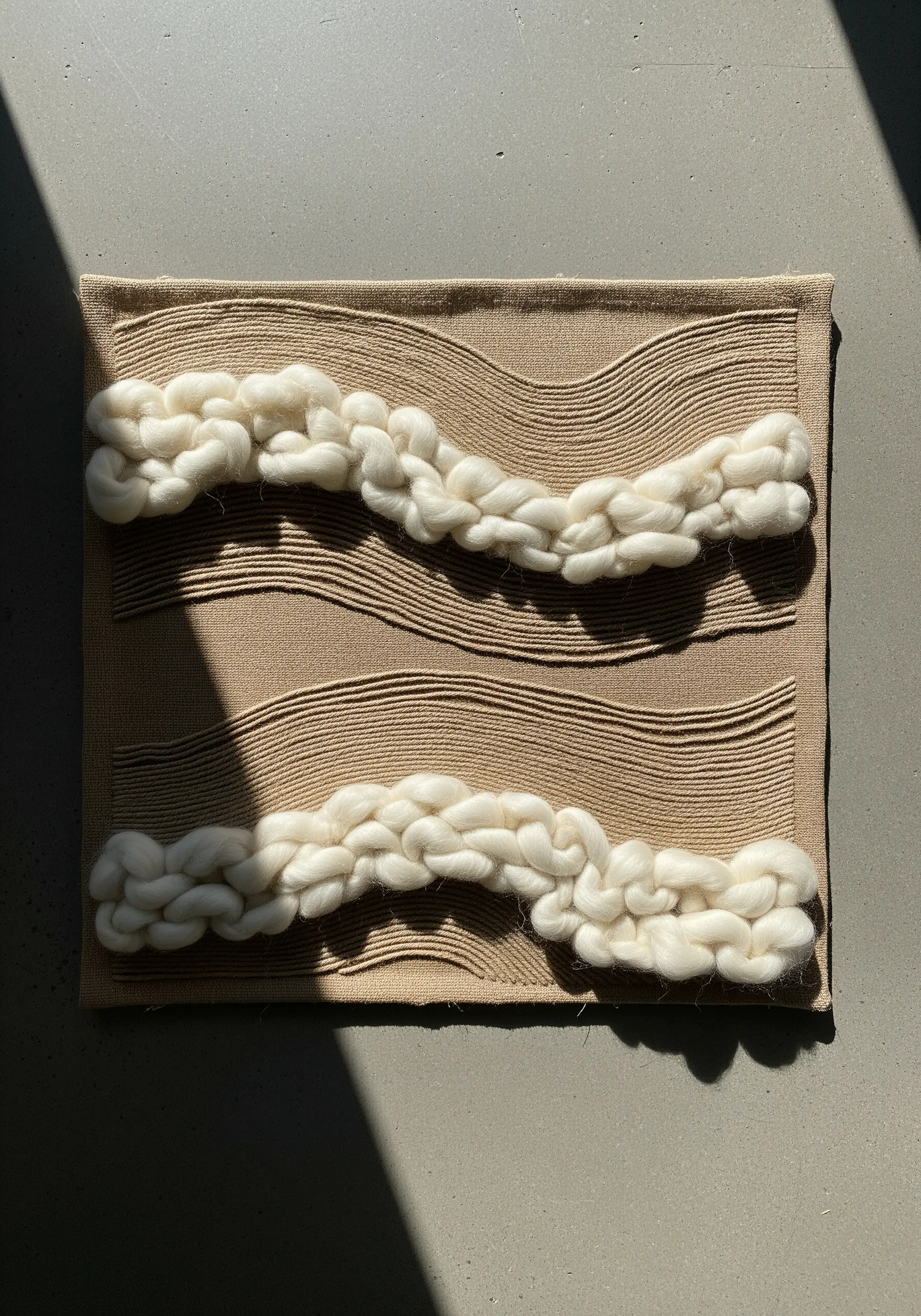 Minimalist textile art with chunky cream wool roving on a beige canvas.