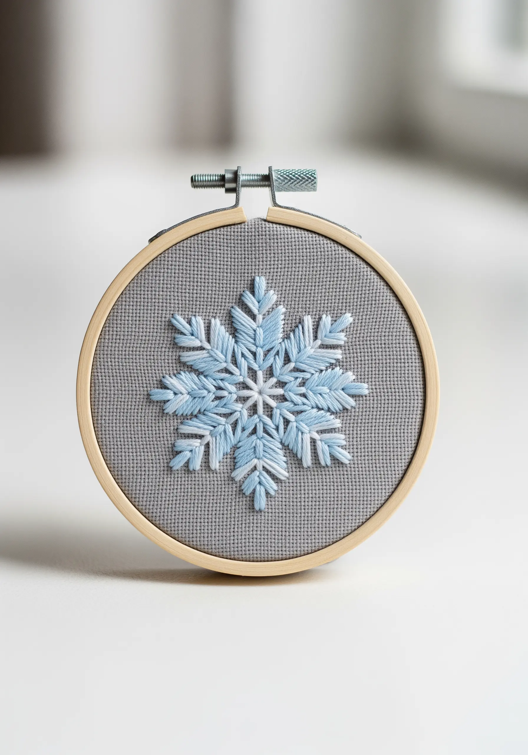 A blue and white embroidered snowflake mandala on grey Aida cloth.