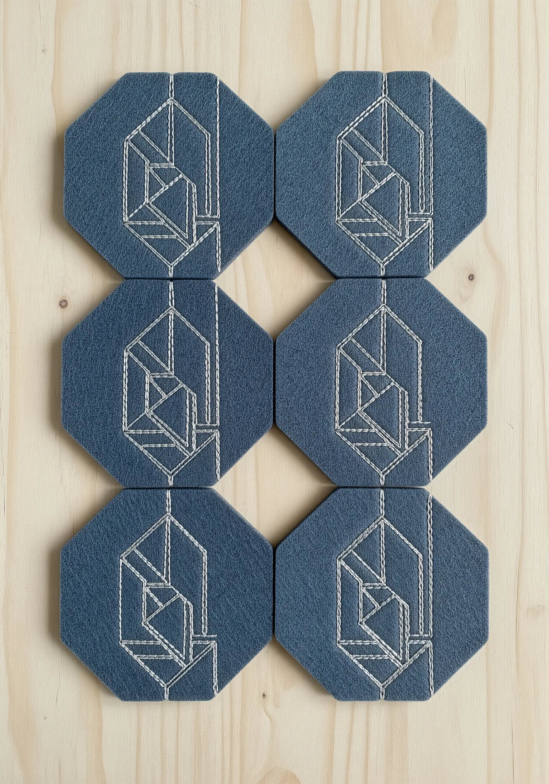 A set of six octagonal coasters with white geometric leaf designs embroidered on blue felt.