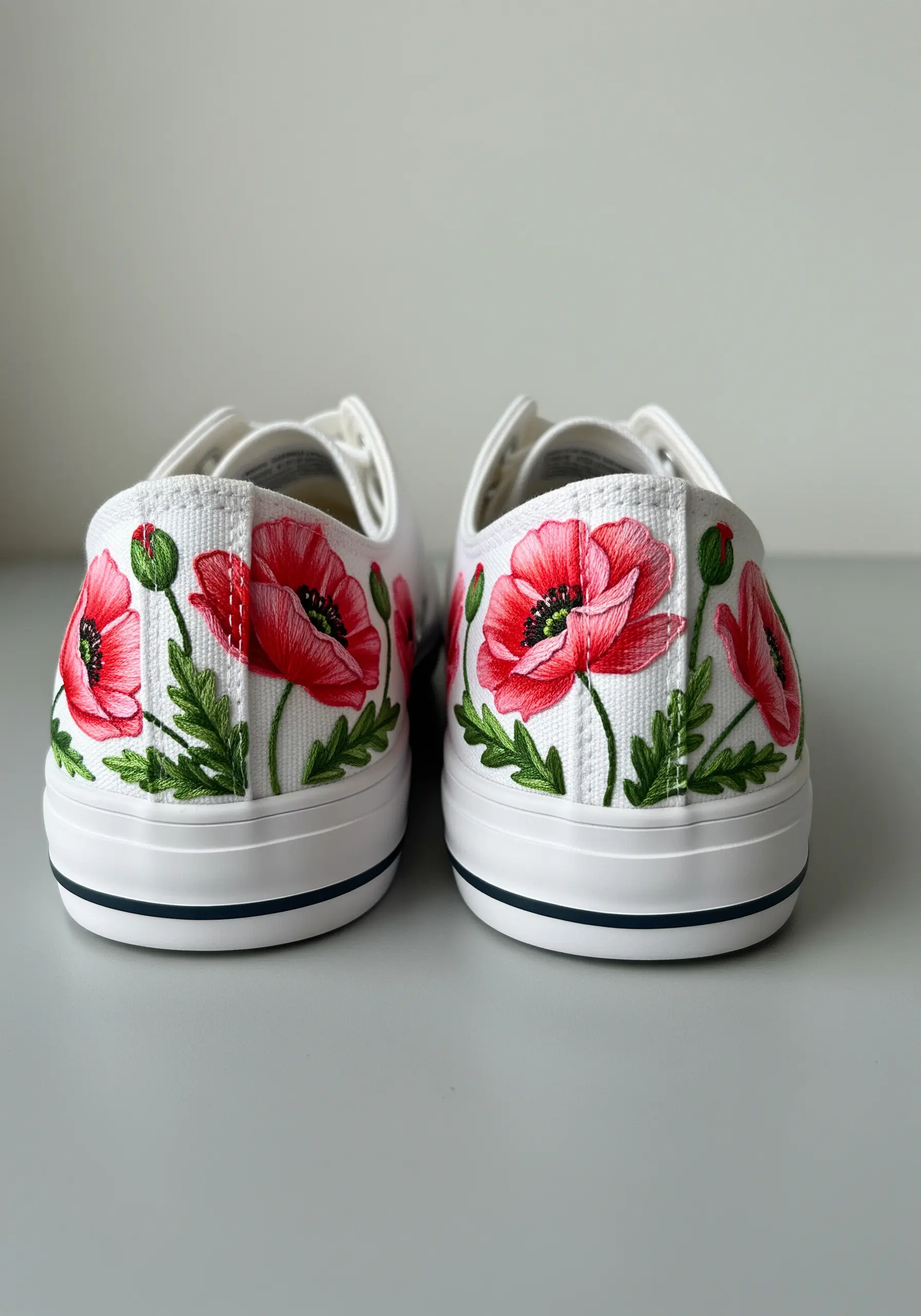 White canvas sneakers with vibrant, painterly embroidered red poppies on the heels.