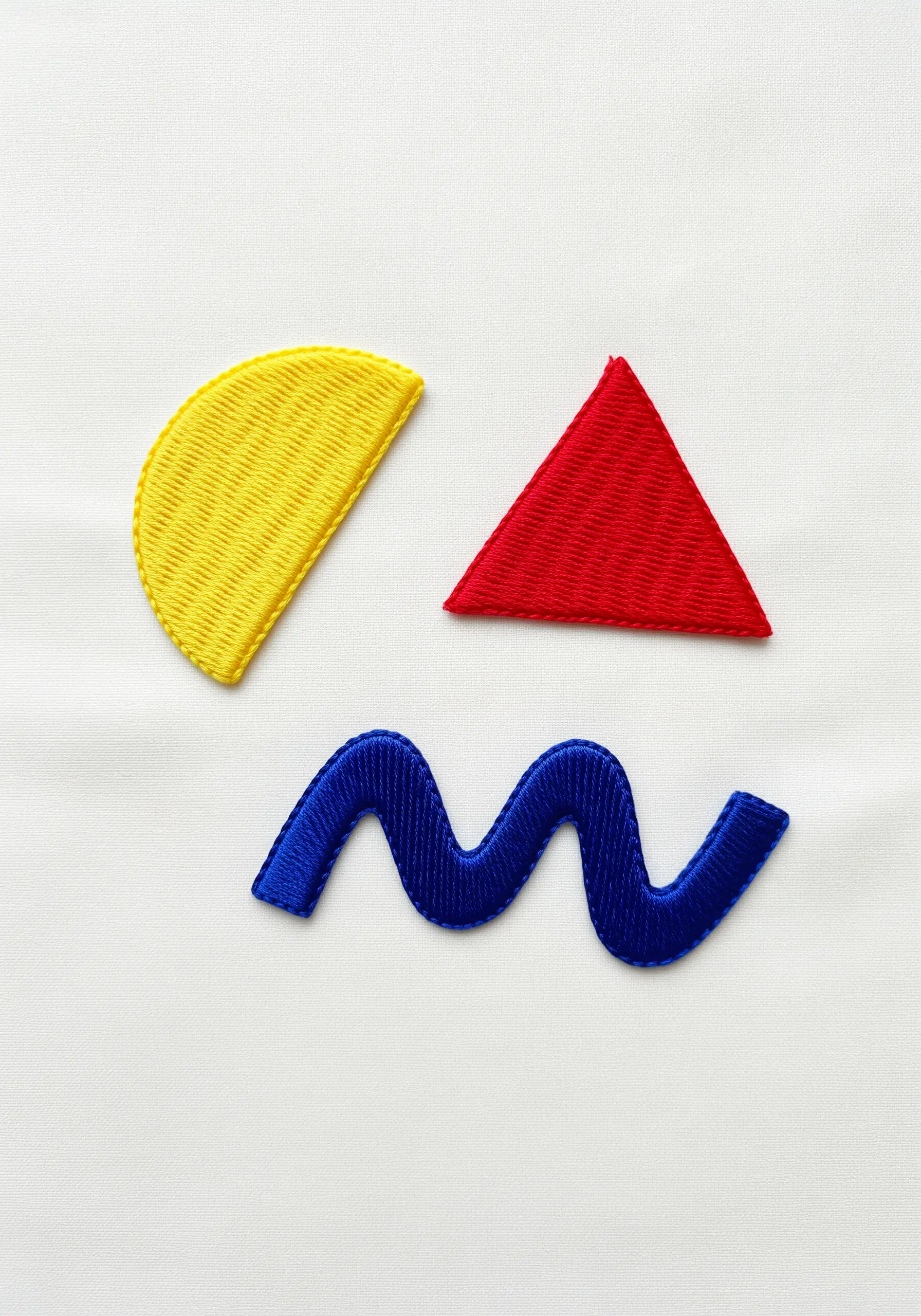 Abstract shapes in yellow, red, and blue satin stitch on white fabric.