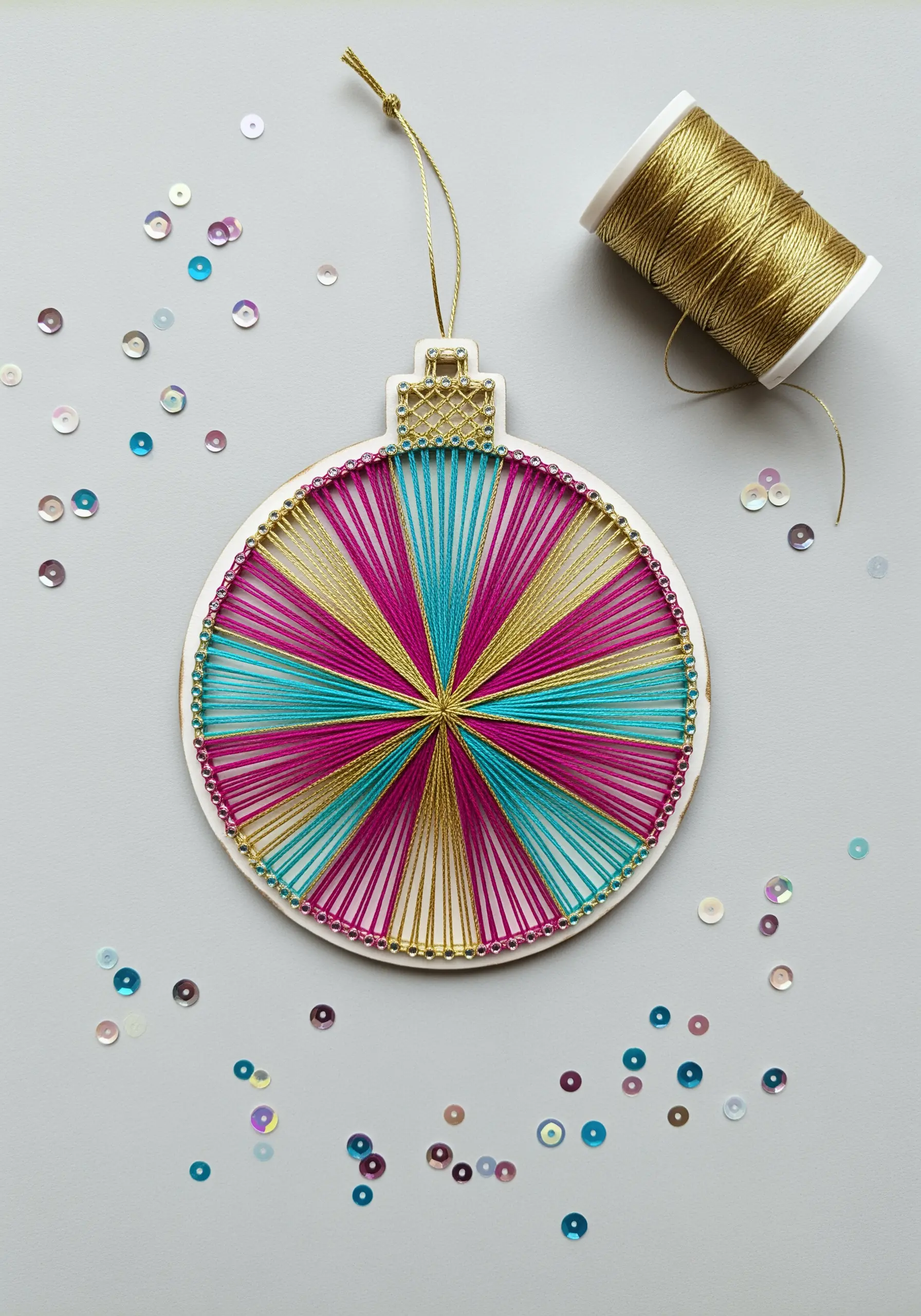 Colorful string art Christmas bauble with sections of pink, blue, and gold.