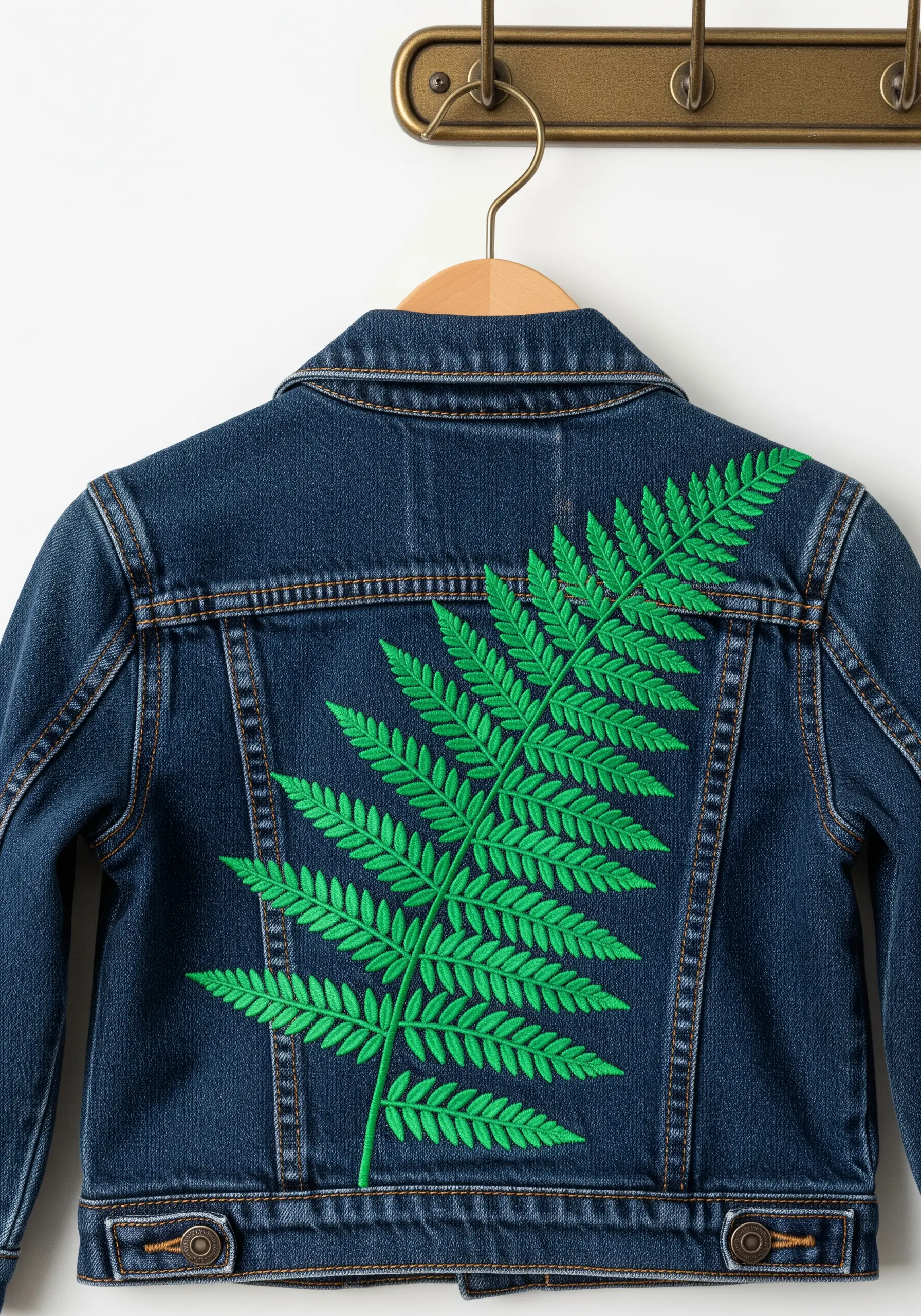 A large, bright green embroidered fern on the back of a children's denim jacket.