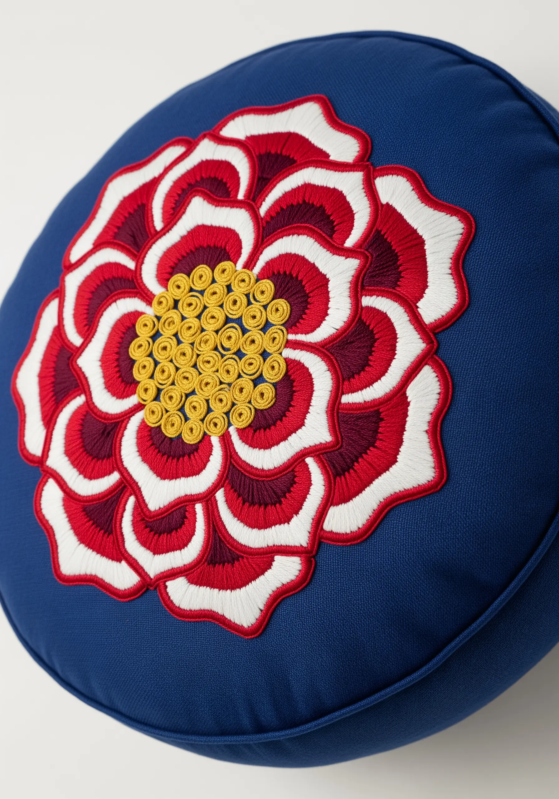 Boldly embroidered red, white, and yellow Tudor rose on a round navy blue cushion.
