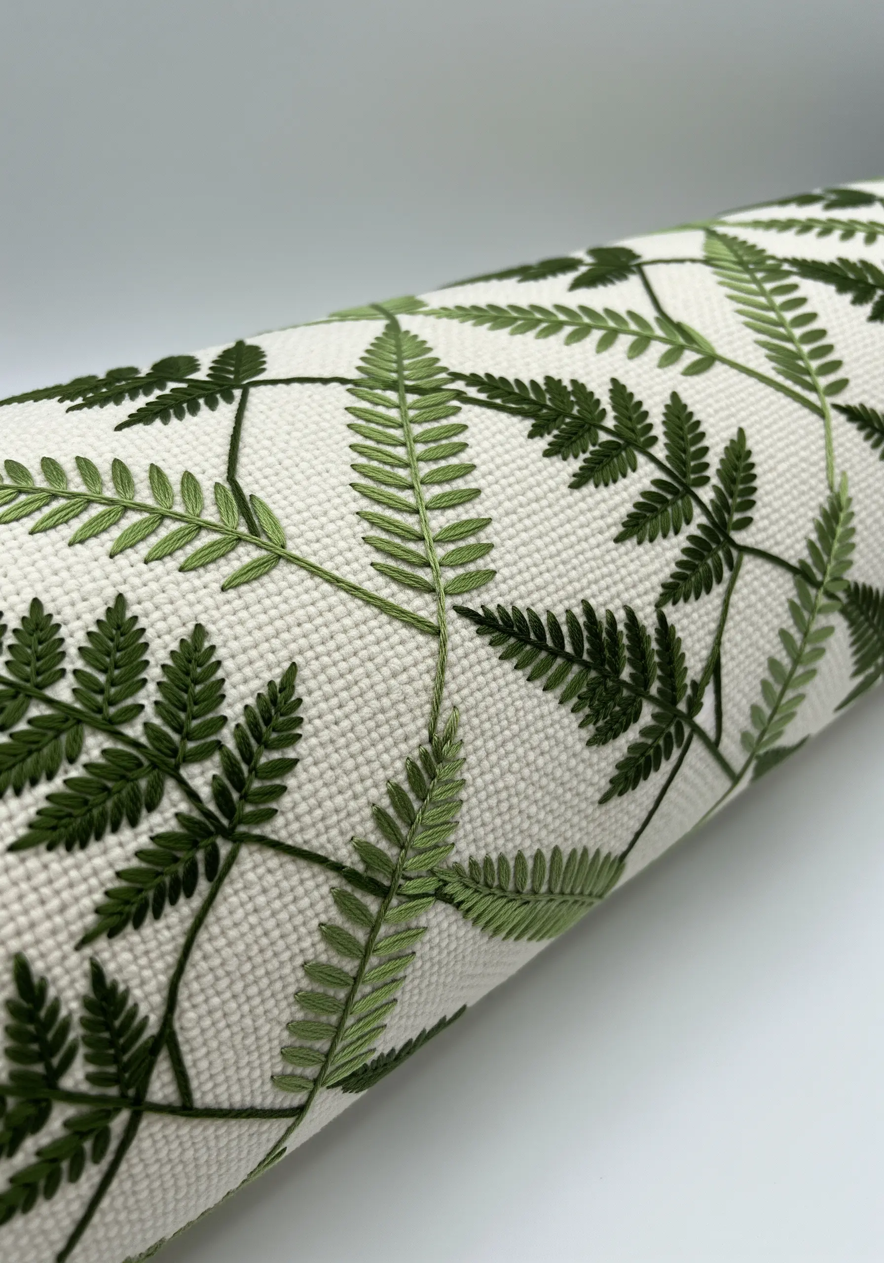 A scatter pattern of delicate green fern leaves embroidered on a textured off-white fabric.