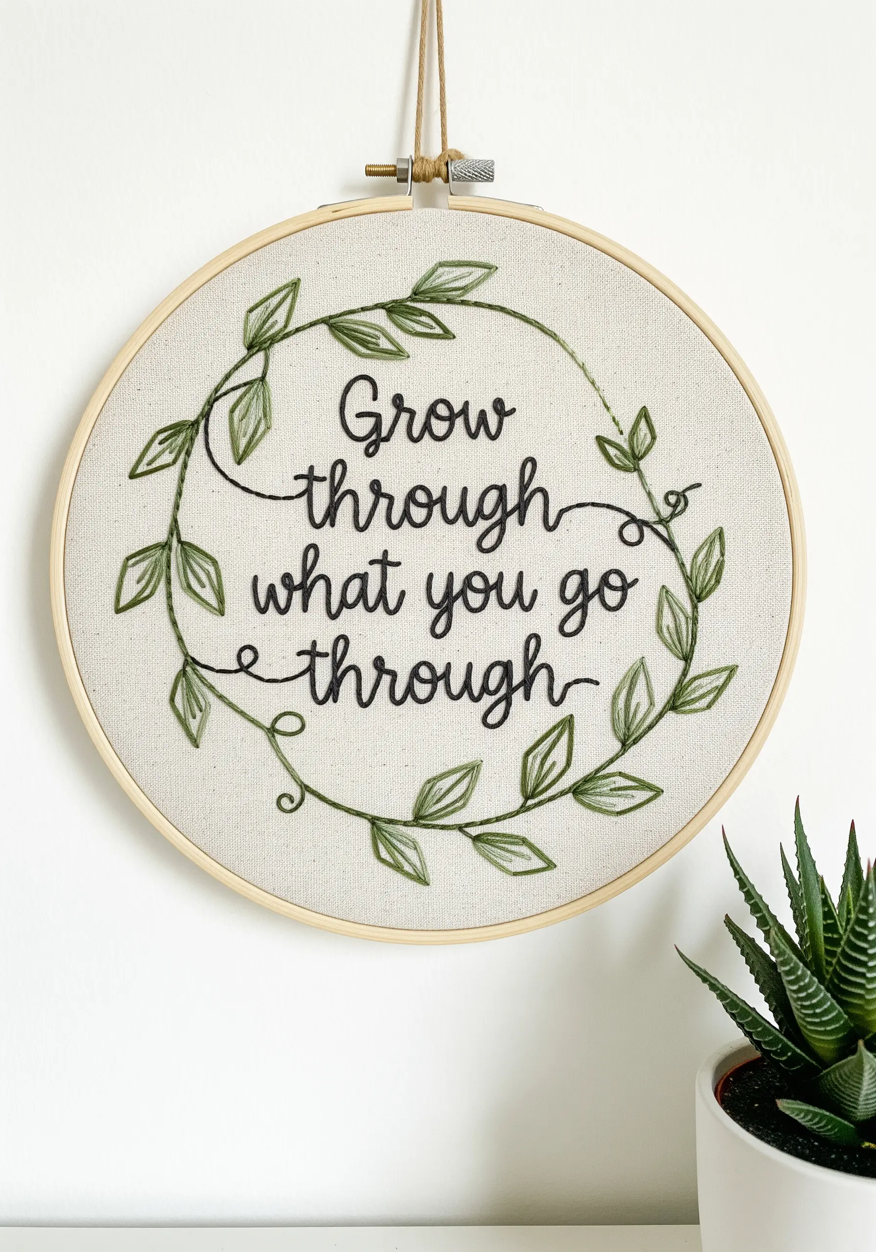 Embroidered quote with a watercolor-effect leafy vine on neutral fabric.