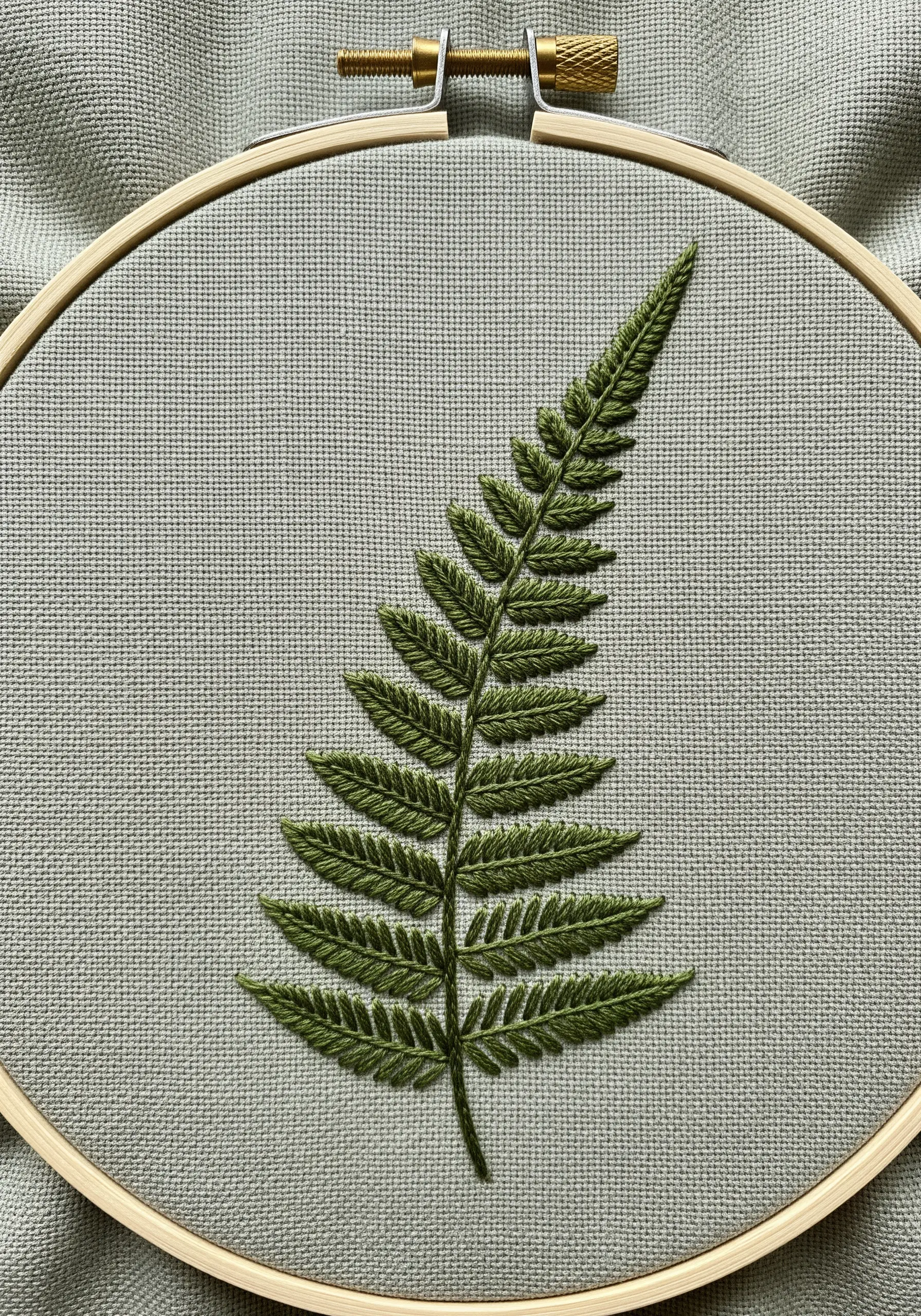 A realistic fern leaf created with detailed fishbone stitch in two shades of green.