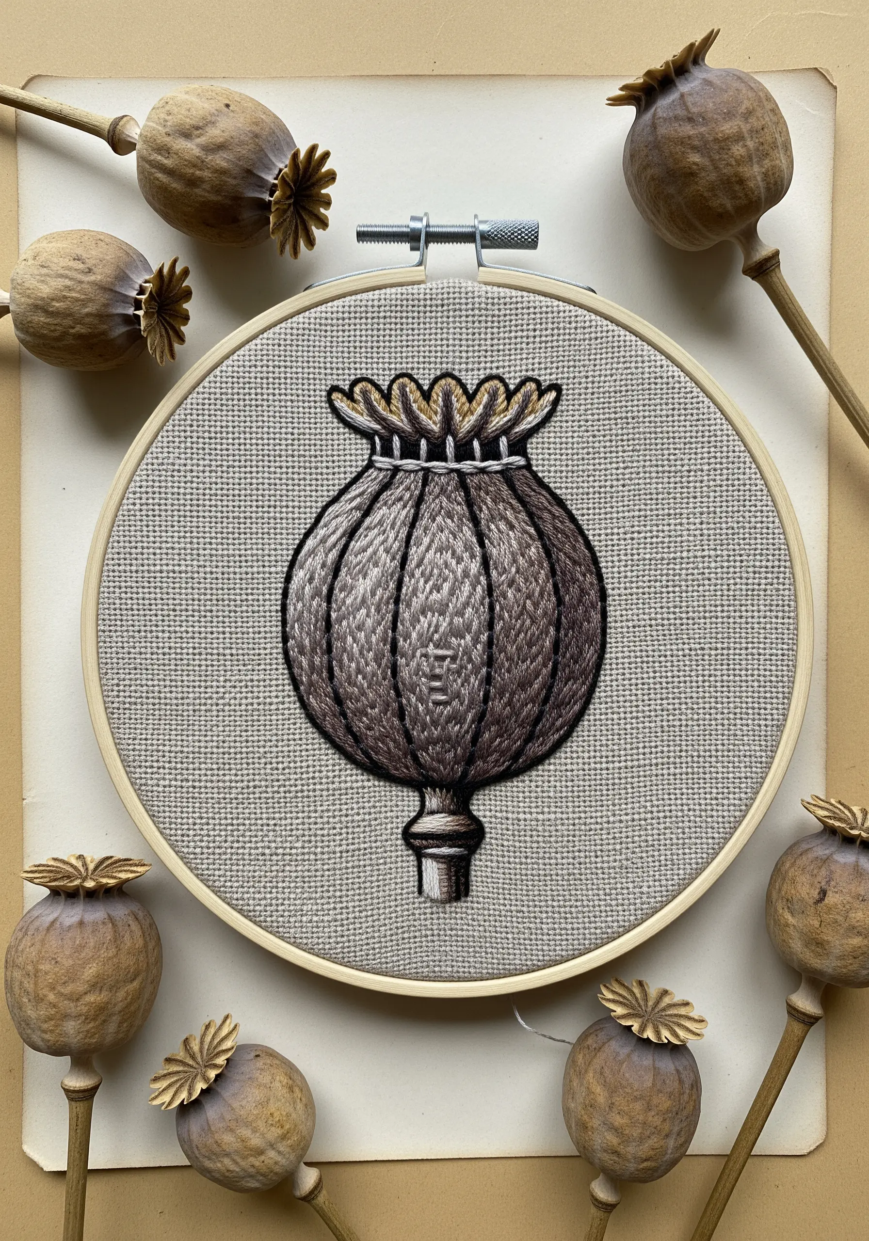 An embroidered poppy seed head with detailed thread painting and a dark black outline.