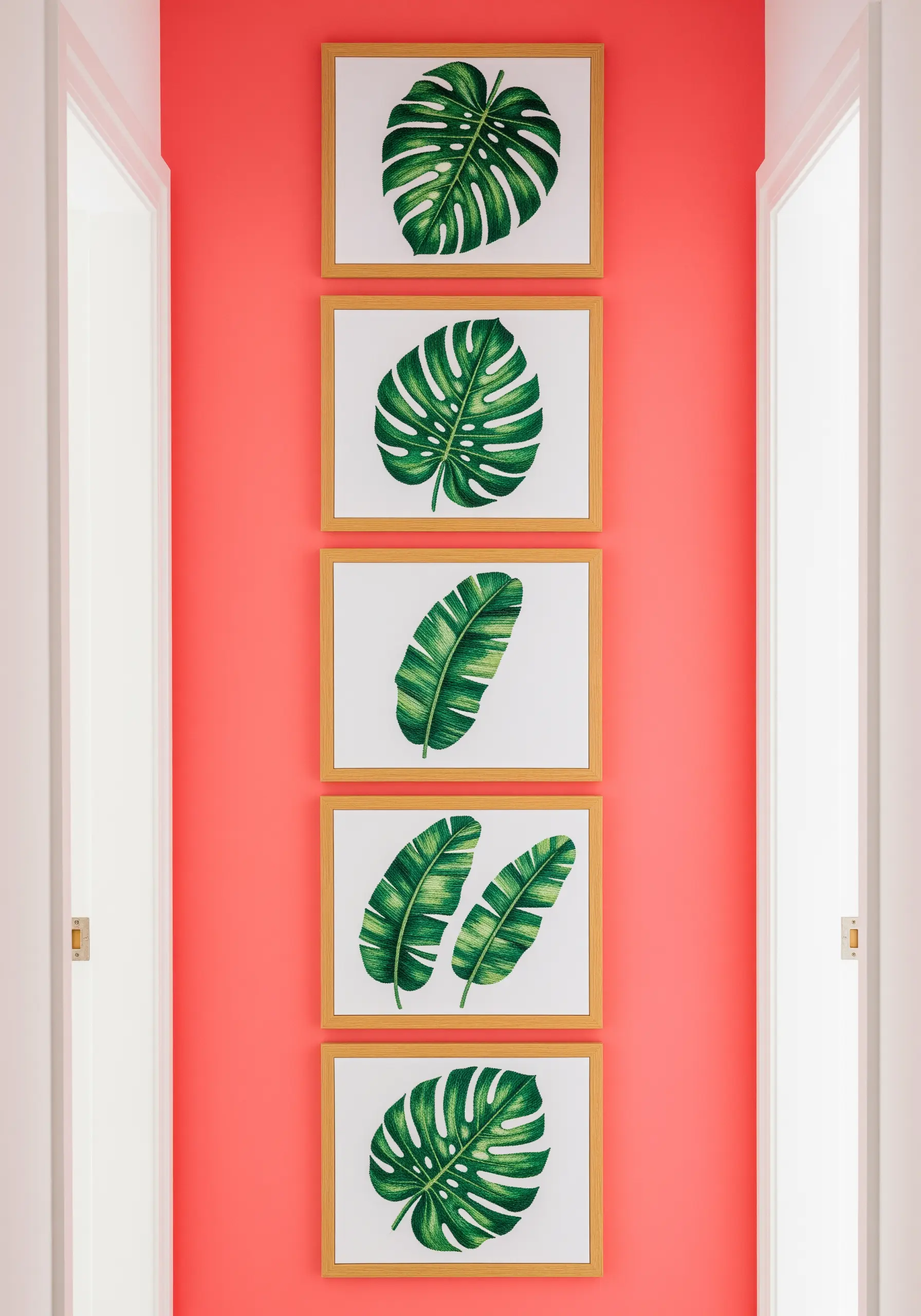 A vertical series of five framed embroideries of tropical leaves on a bright coral wall.