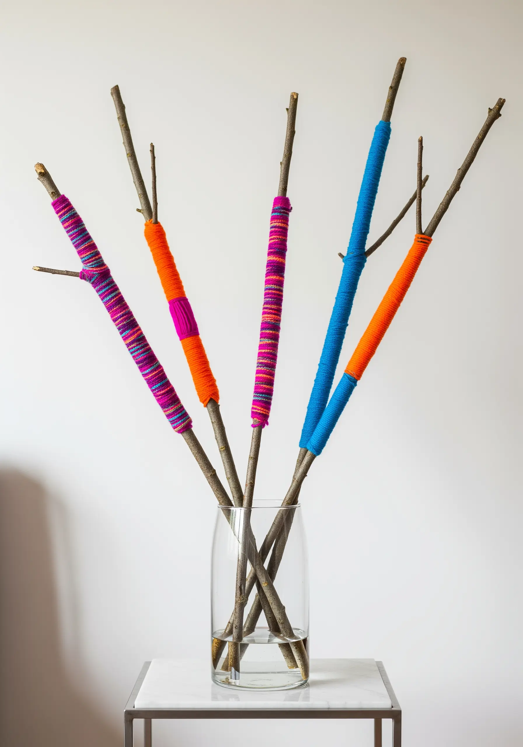 Several dried branches wrapped in sections of bright blue, orange, and pink yarn.