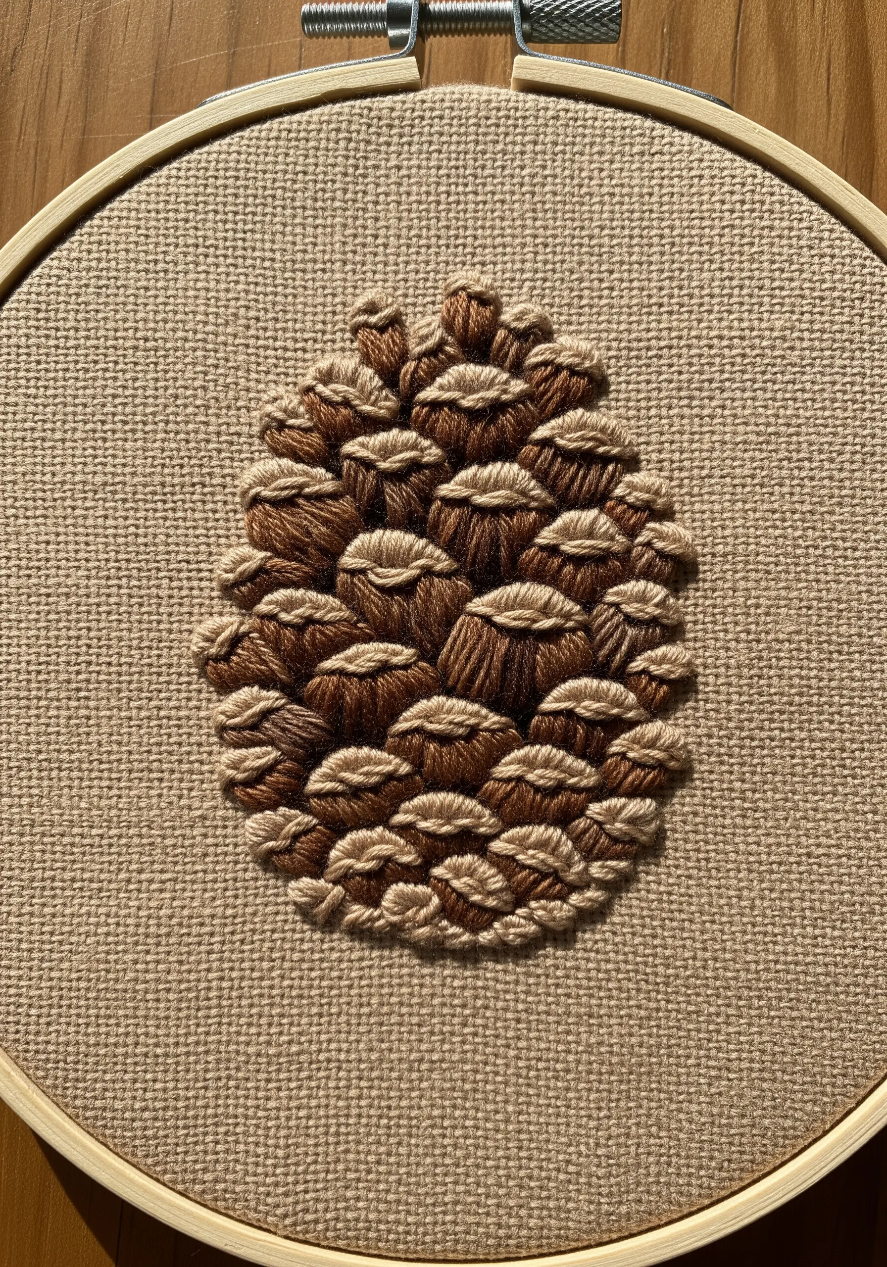 A highly textured, layered embroidery of a pinecone using various brown threads.