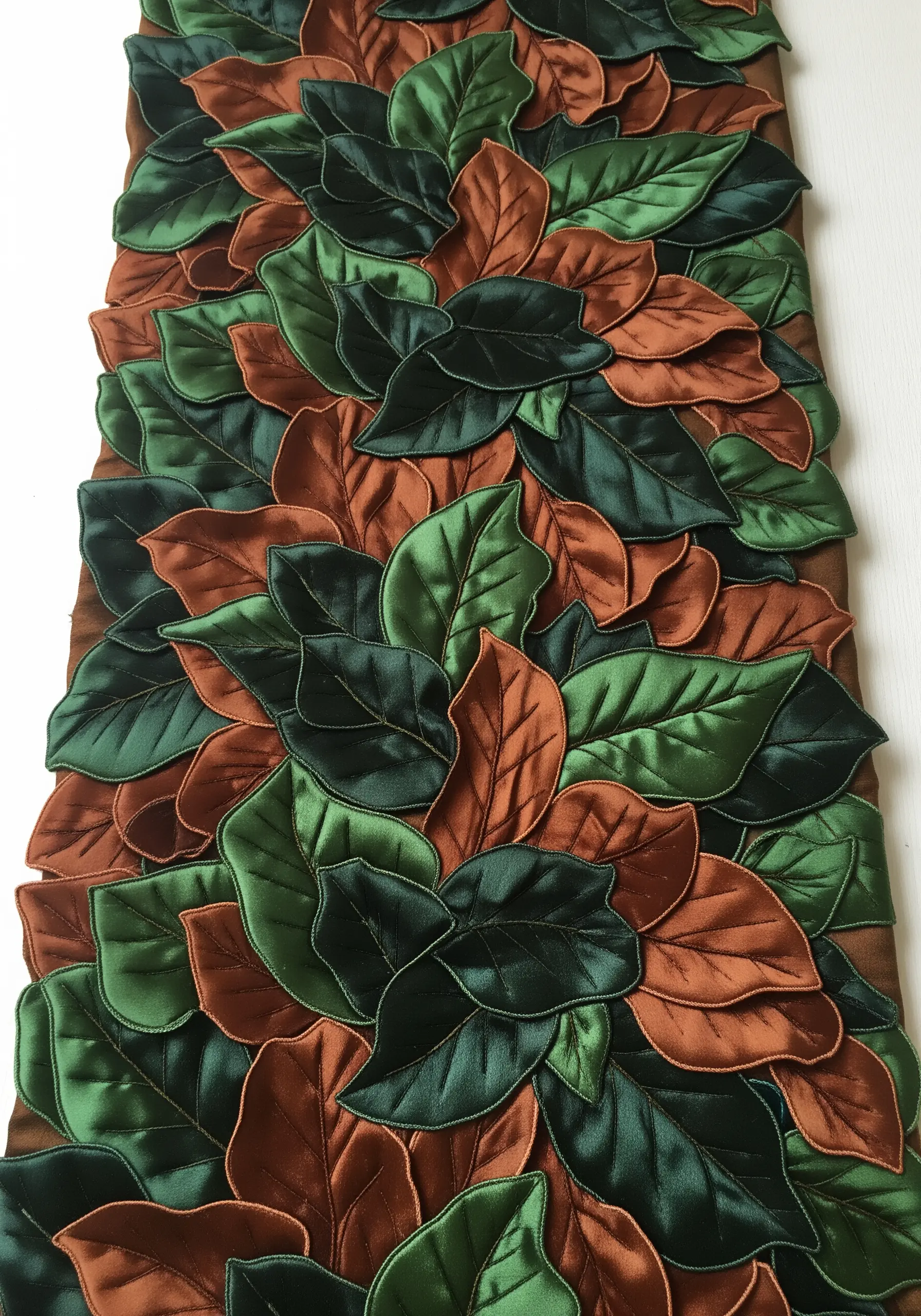 A dense table runner covered in overlapping, three-dimensional fabric leaves in green and brown.