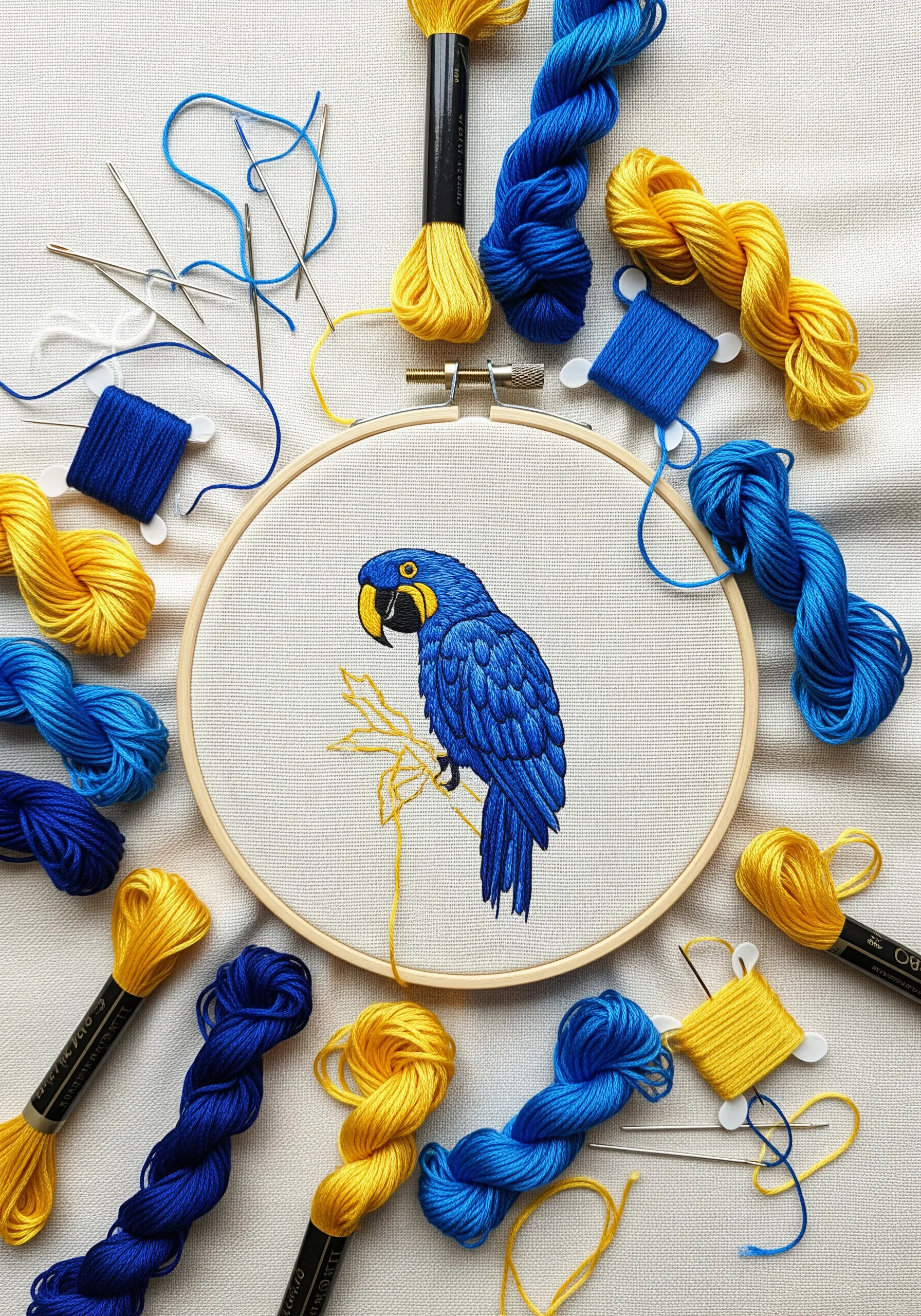 A blue hyacinth macaw embroidered in a hoop, surrounded by spools of blue and yellow thread.