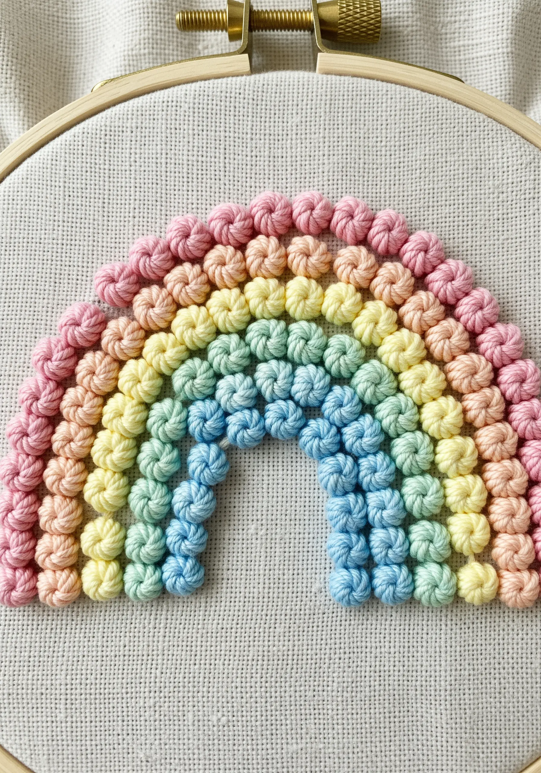 A pastel rainbow made of tightly packed, textured knots on neutral fabric.
