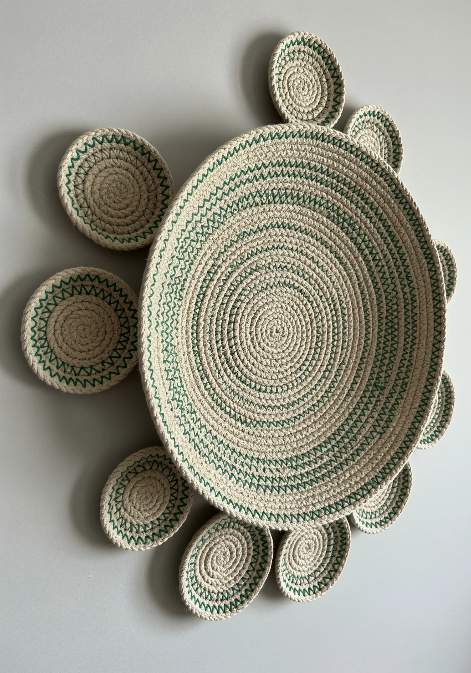 A wall installation of coiled rope bowls in various sizes, stitched with green thread.