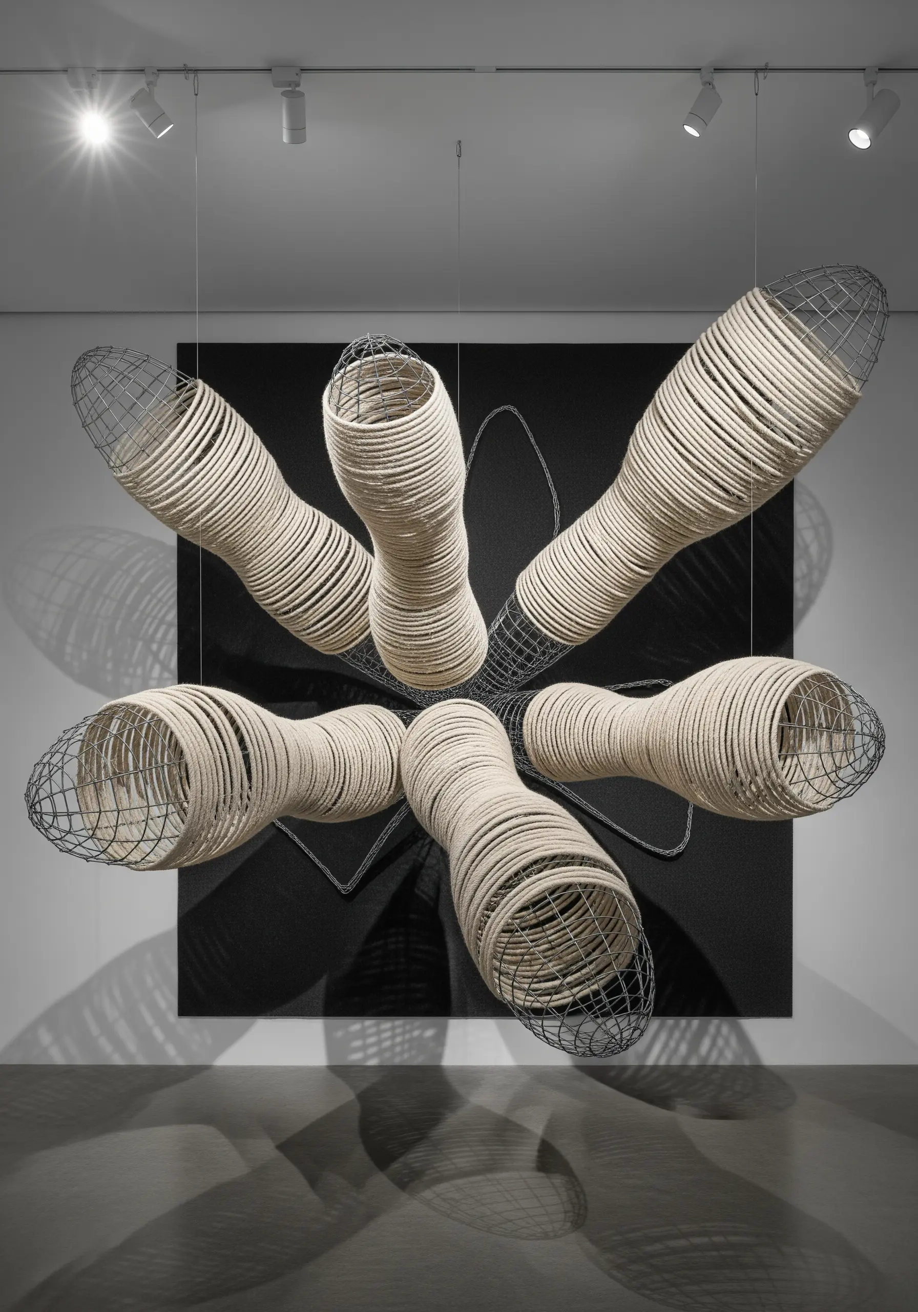 A large suspended sculpture made of wireframes wrapped tightly with off-white rope.