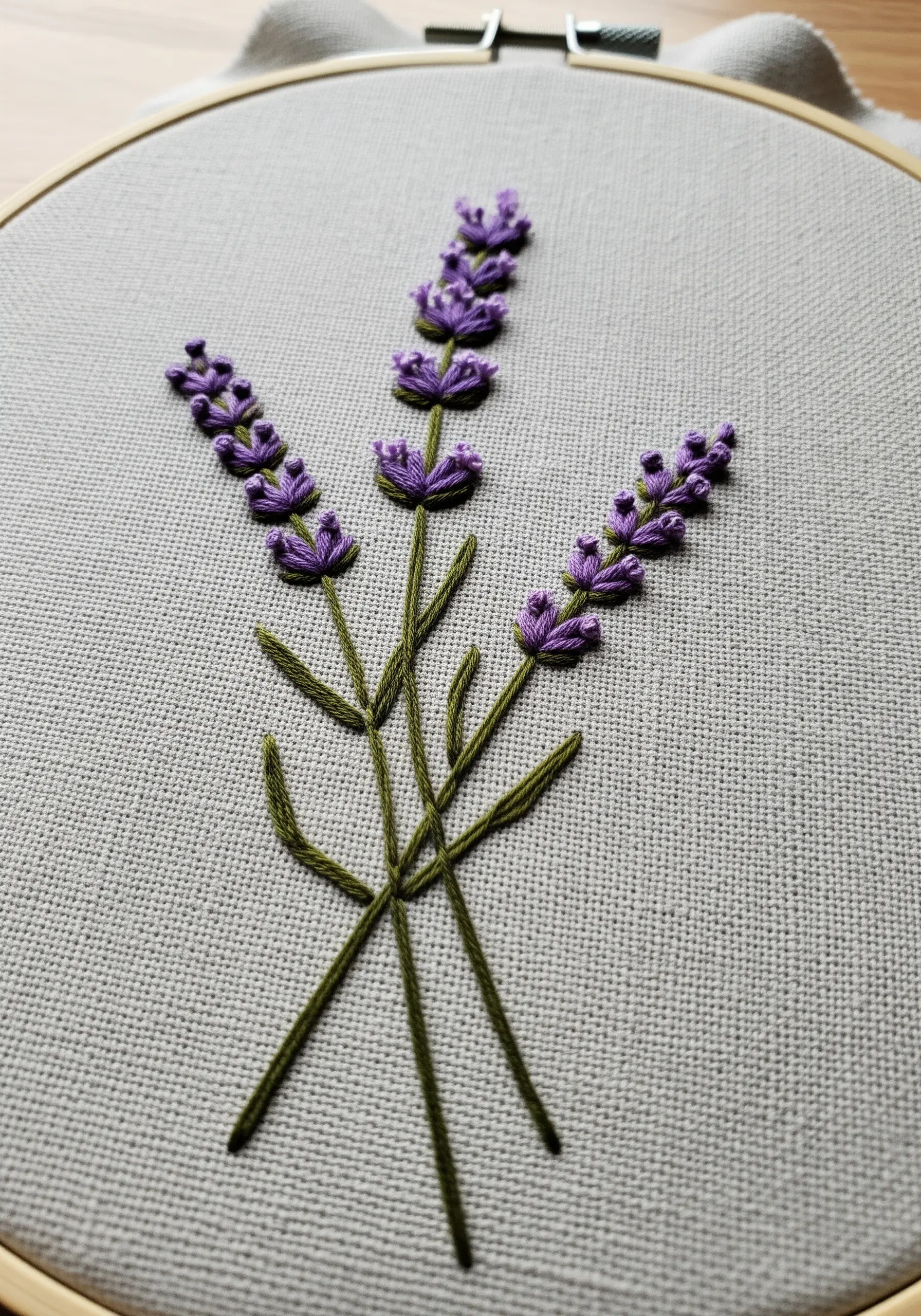 Detailed embroidery of three lavender sprigs with purple French knots on gray fabric.