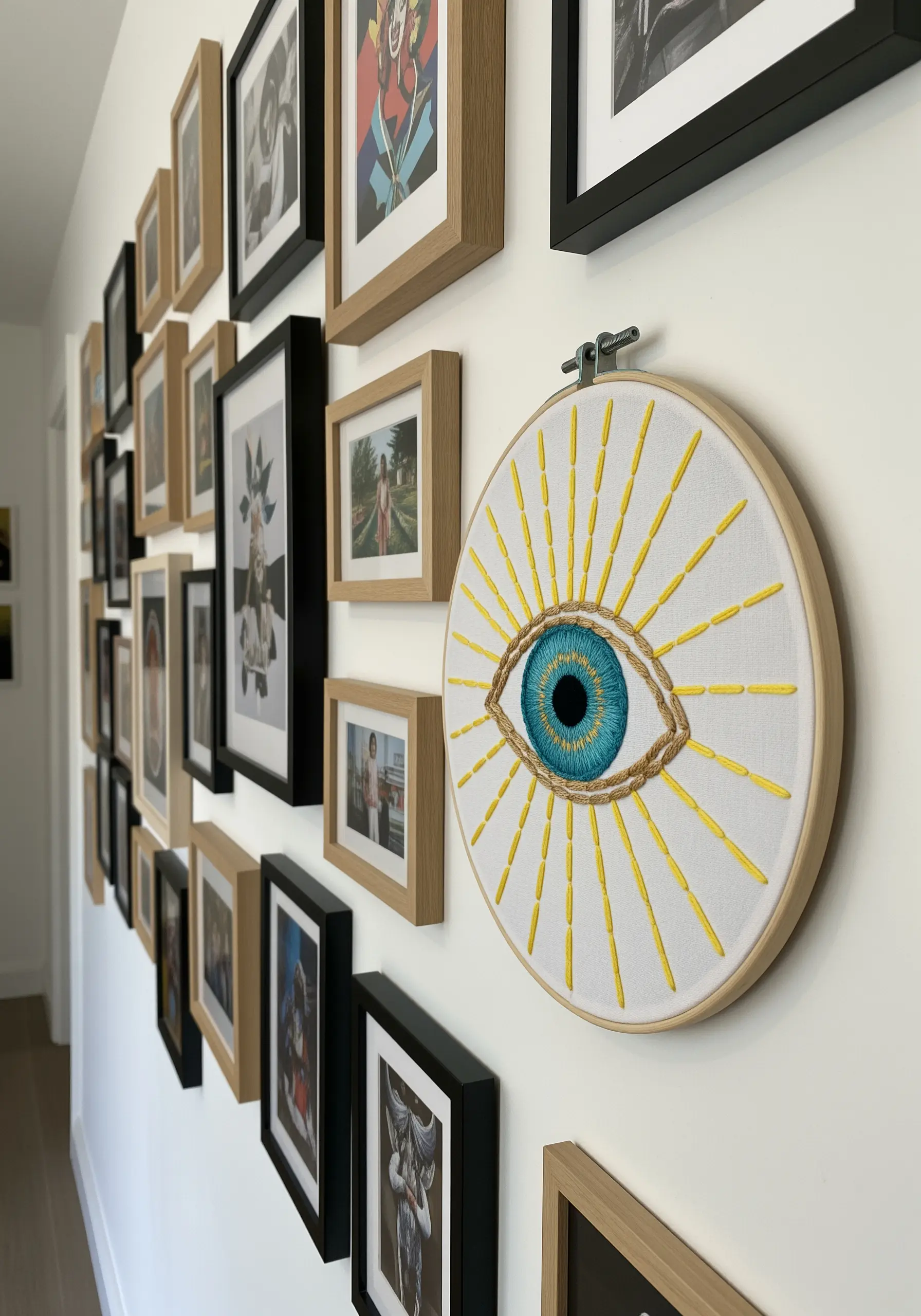 A large embroidery hoop of an evil eye with bright yellow sun rays, hanging on a gallery wall.