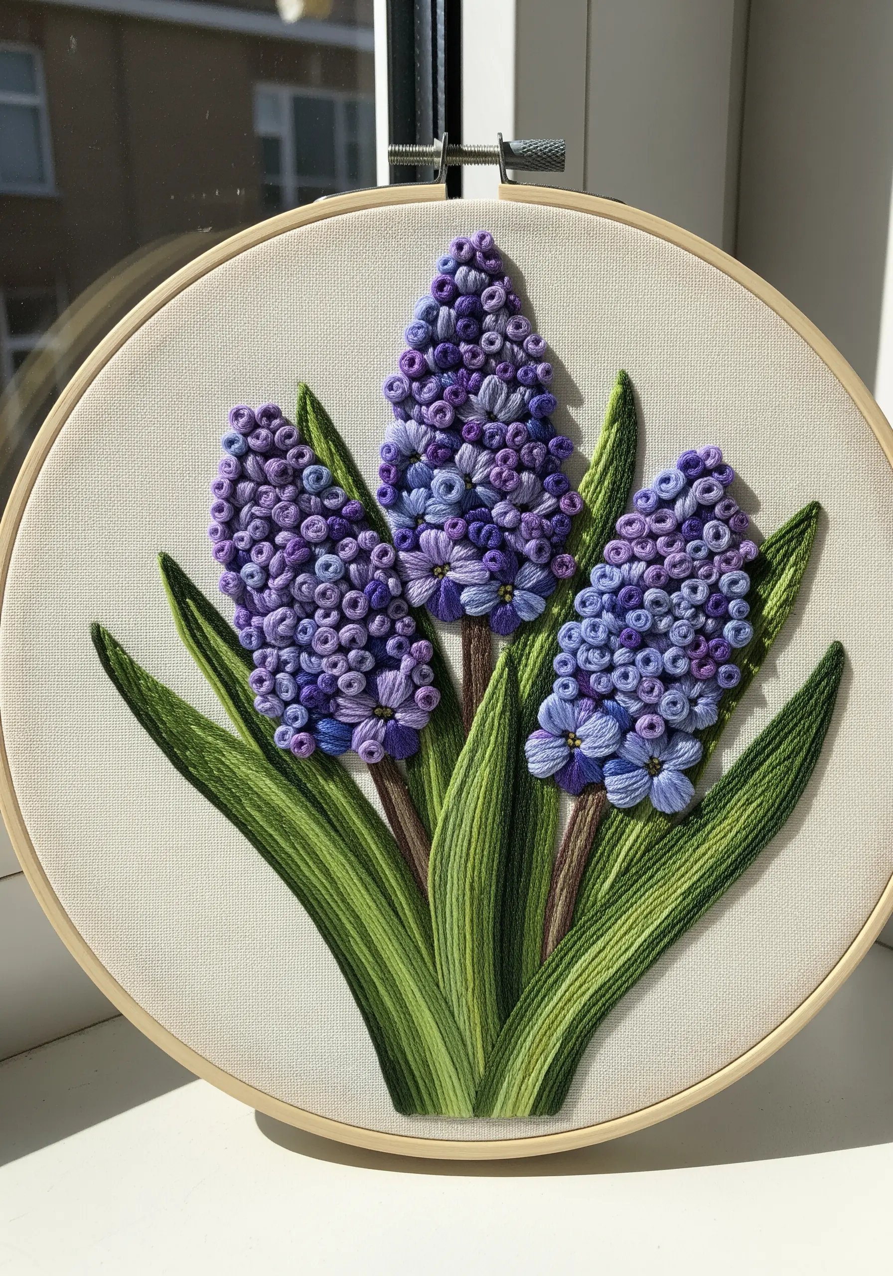 Three embroidered hyacinths with dense purple bullion knots and green leaves.