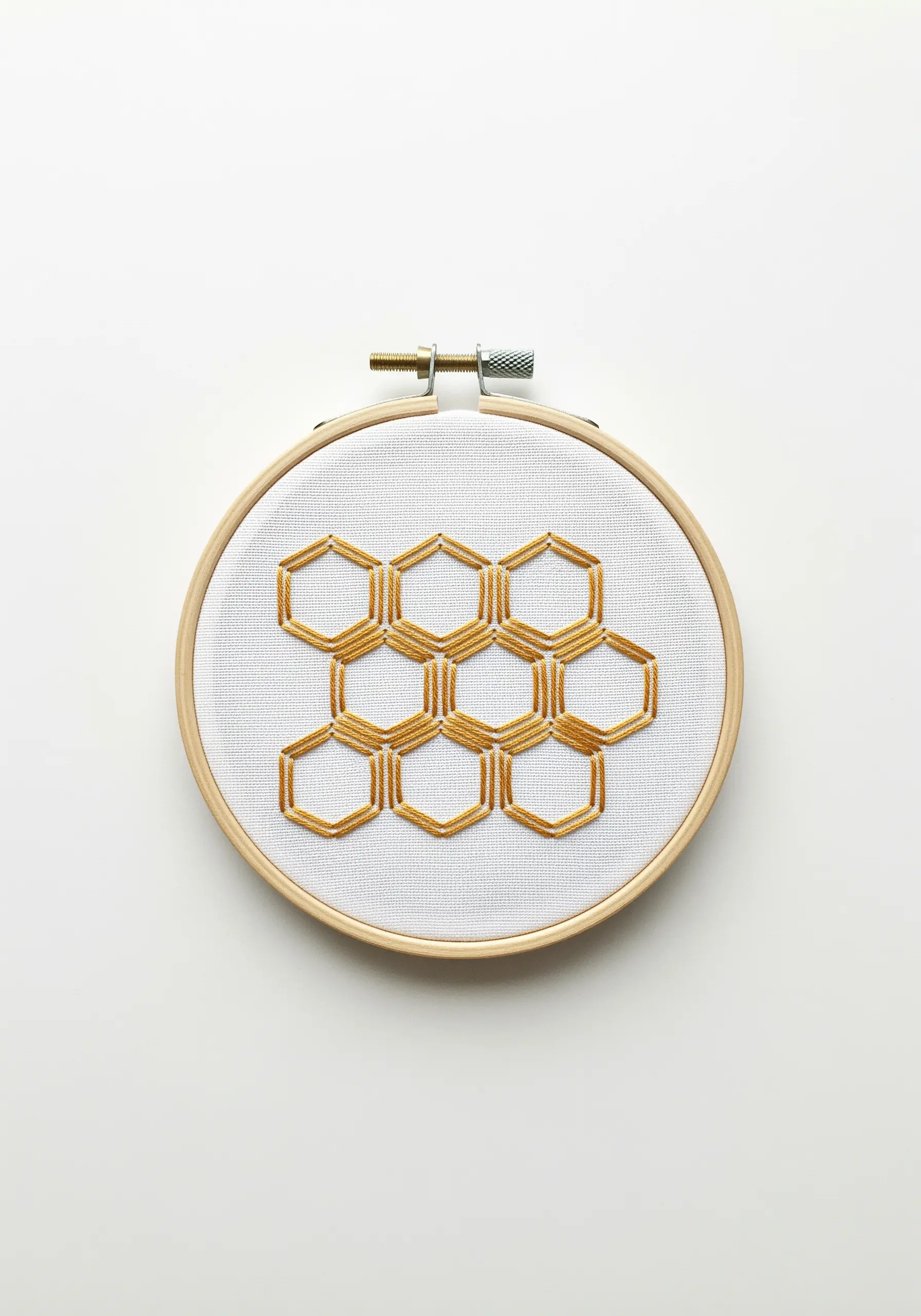 A geometric honeycomb pattern created with golden-yellow open satin stitch on white fabric.
