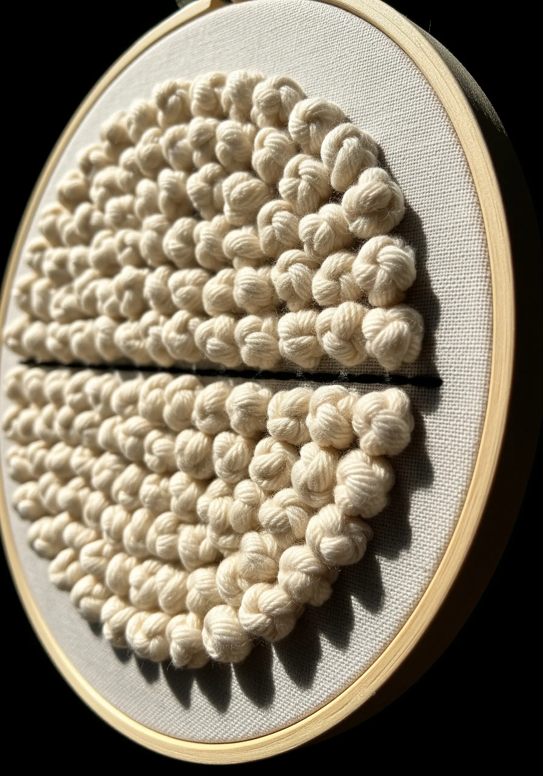 Close-up of a textured circle made of cream-colored Colonial knots on fabric.