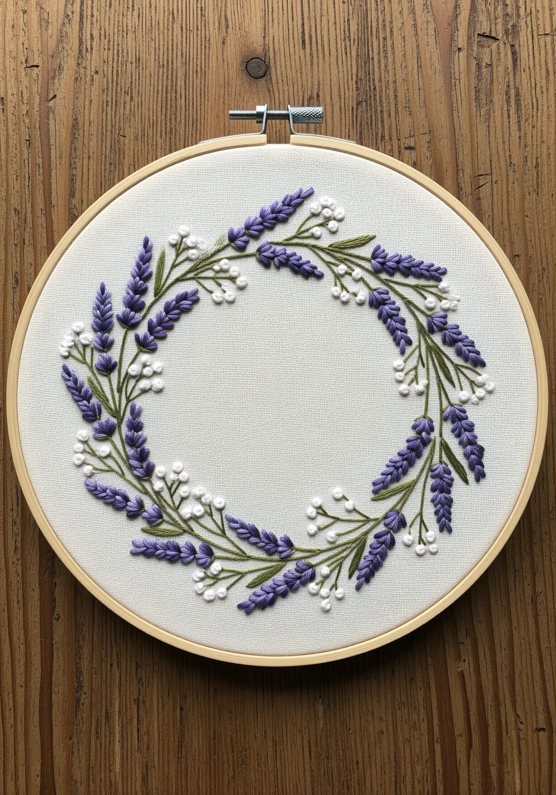An embroidered lavender wreath with textured purple and white flowers on off-white fabric.