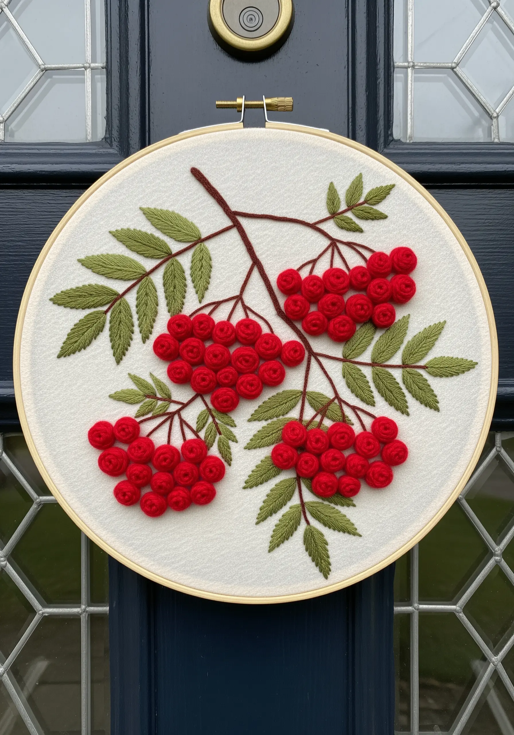 A branch of rowan with clusters of red French knot berries and green fishbone stitch leaves.