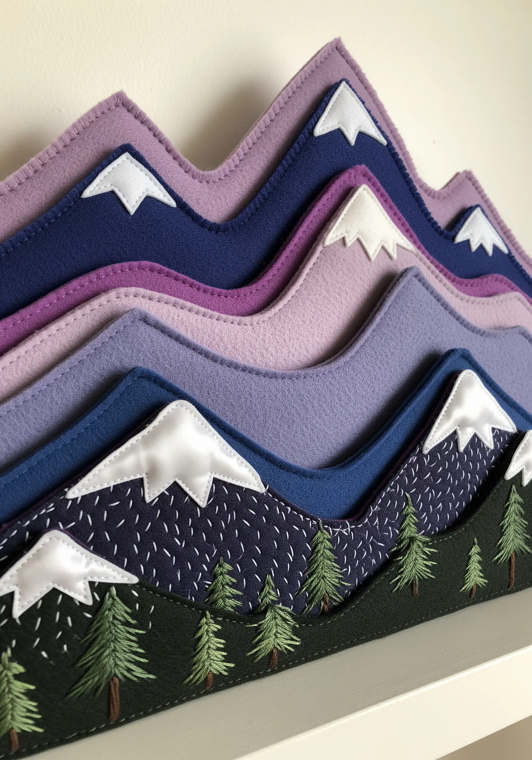 A layered felt wall hanging depicting mountain ranges in shades of purple and blue.