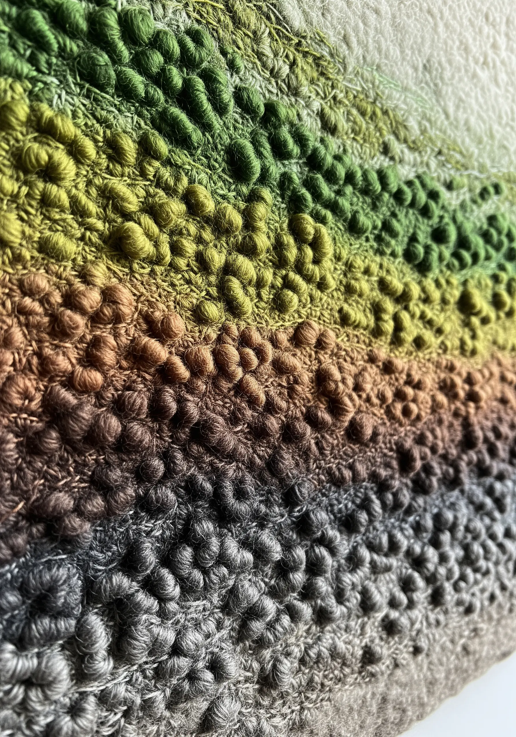 A close-up of a dense, textured surface made of tightly packed French knots in an earthy gradient.