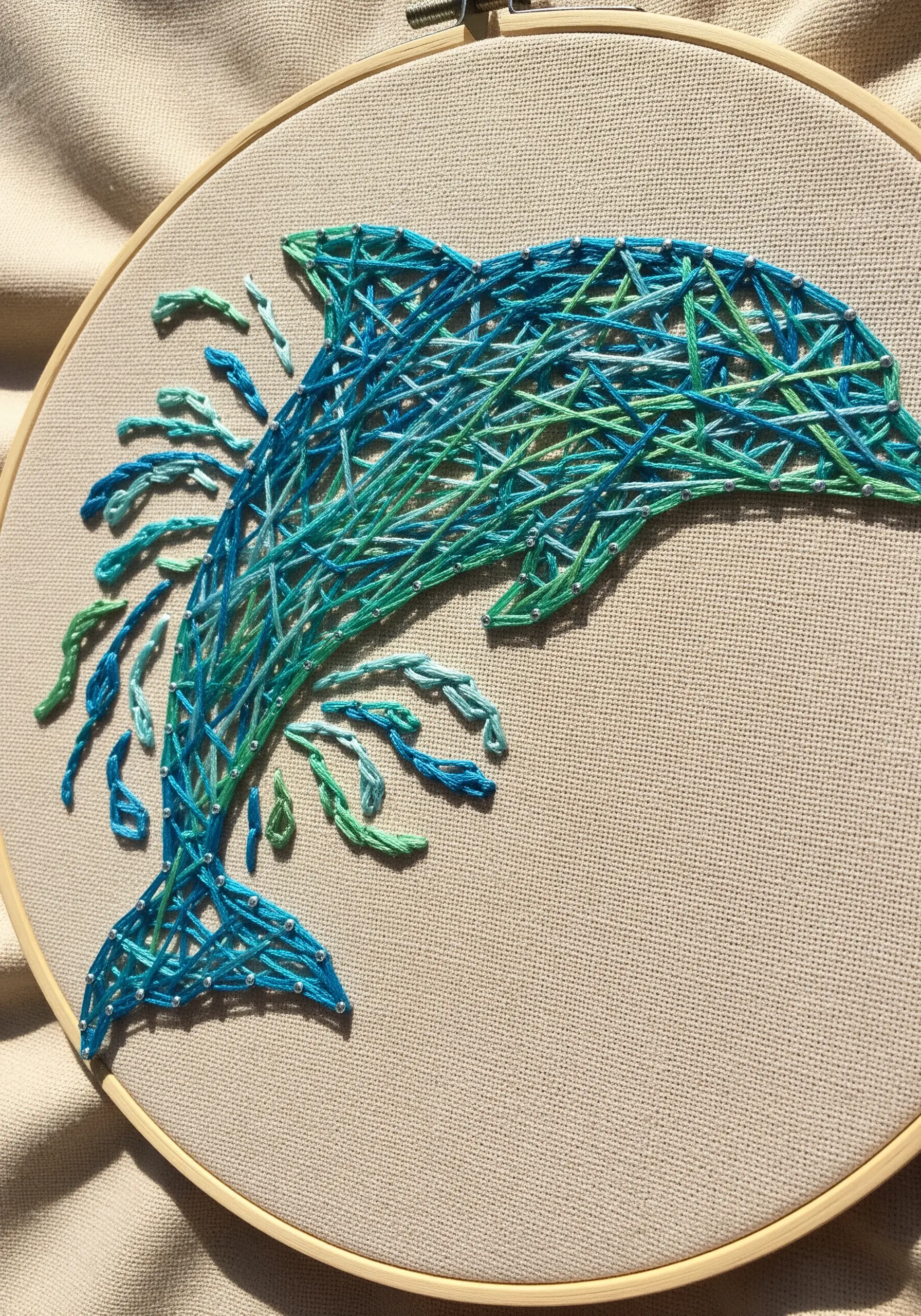 Embroidered dolphin with blue and green stitches, creating a splashing water effect.
