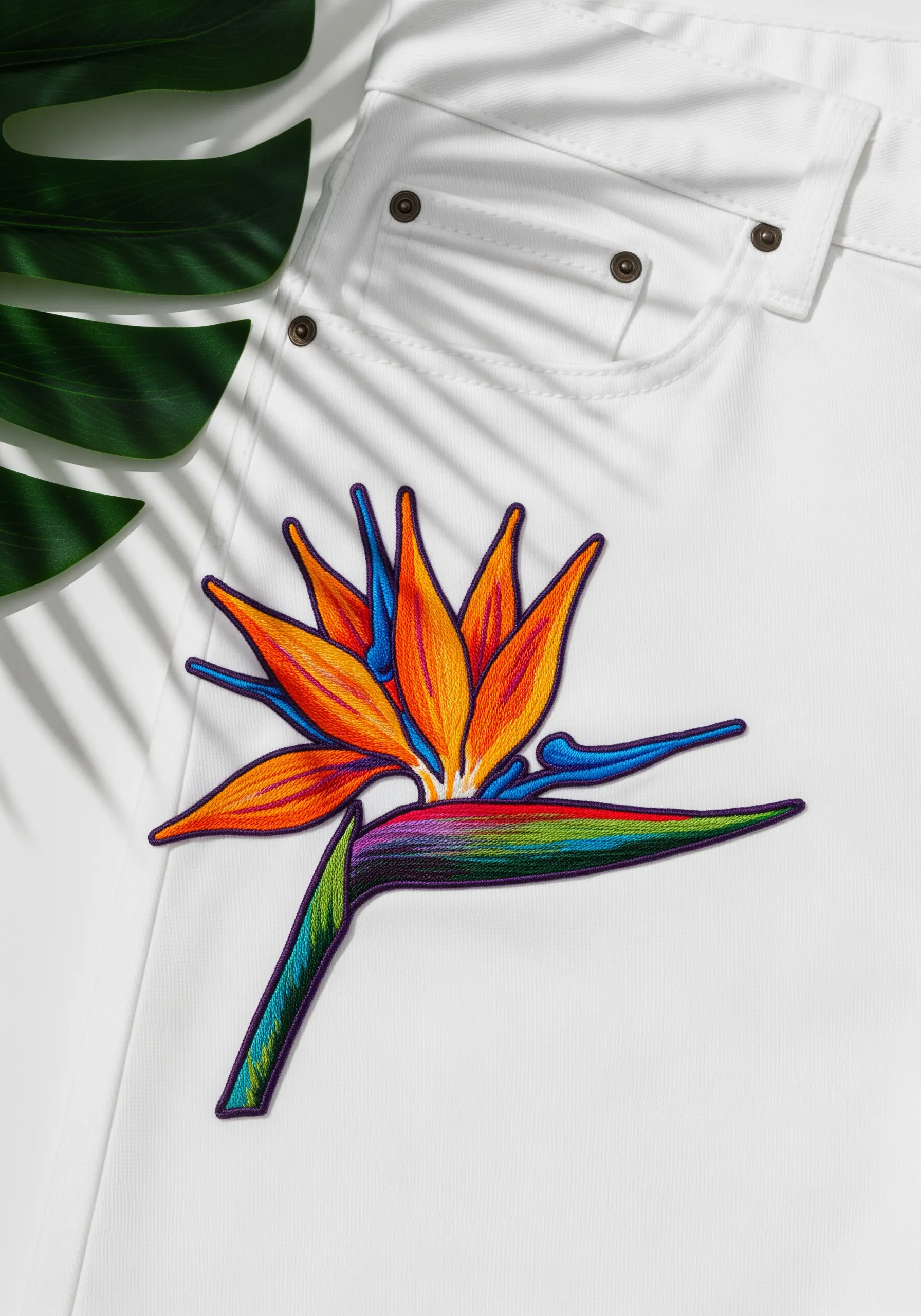 A vibrant Bird of Paradise flower patch with blended orange, blue, and green on white jeans.
