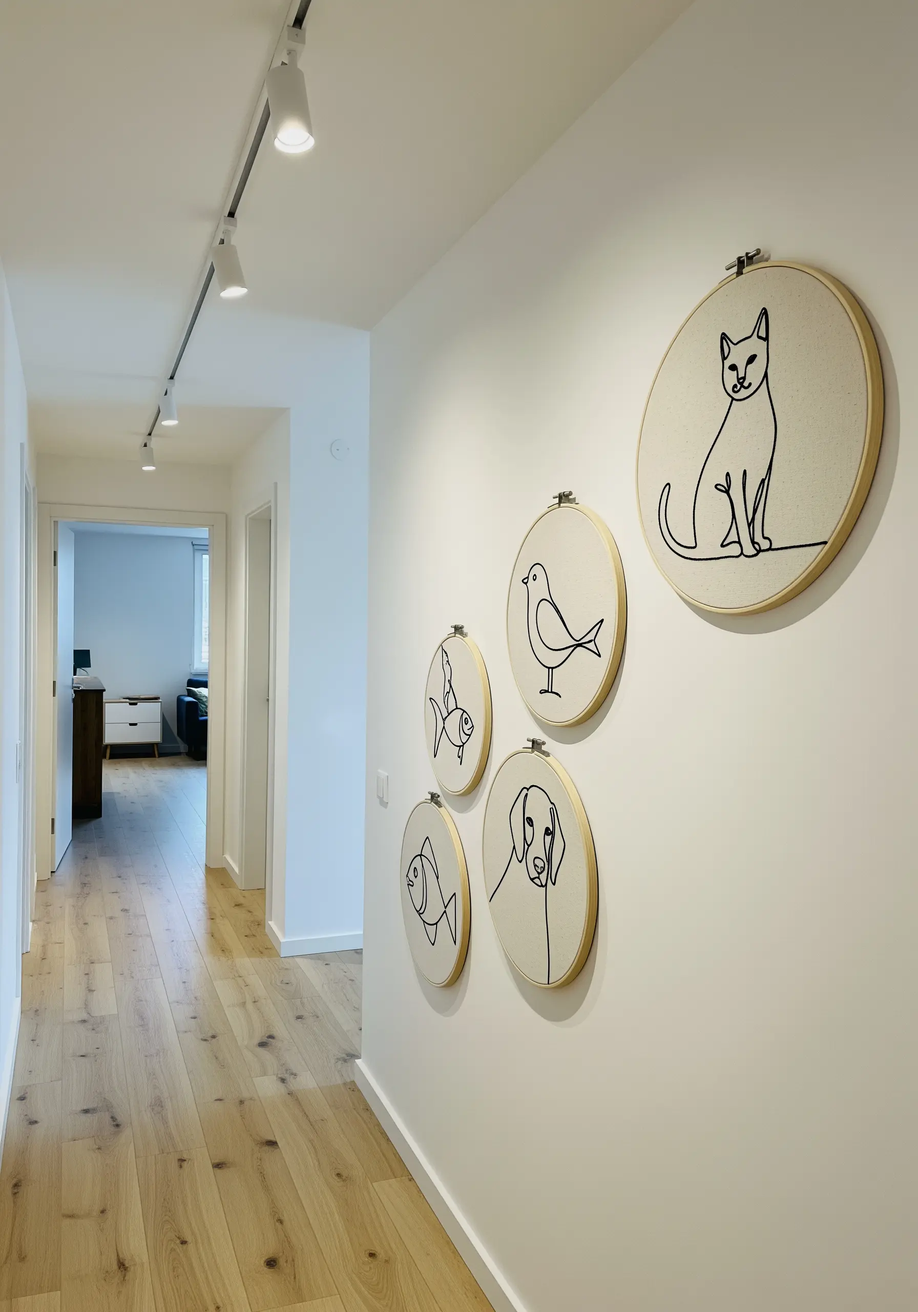 A collection of single-line art pet portraits embroidered in hoops on a hallway wall.