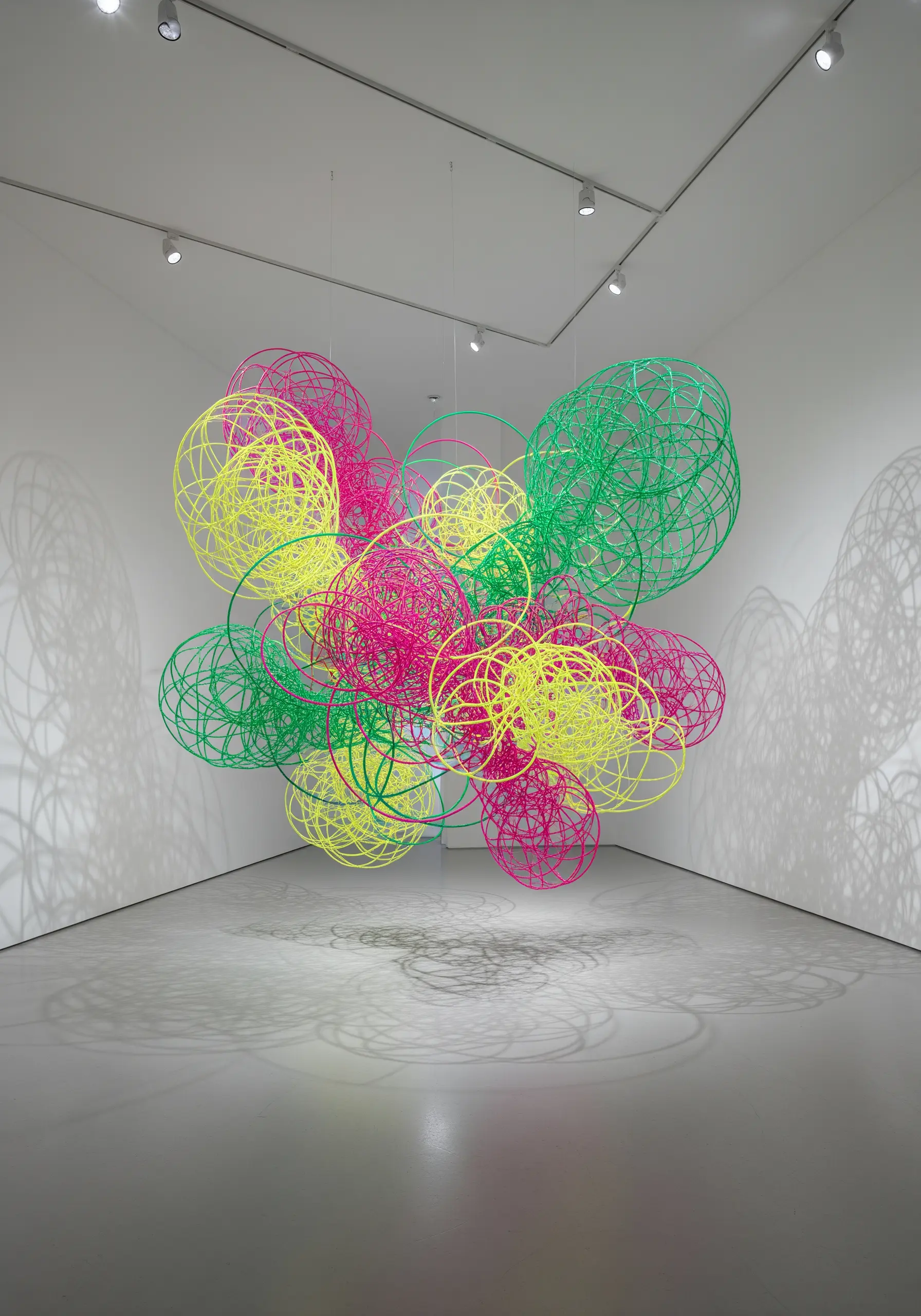 A chaotic cluster of neon pink, green, and yellow circular shapes made of thread-wrapped wire.