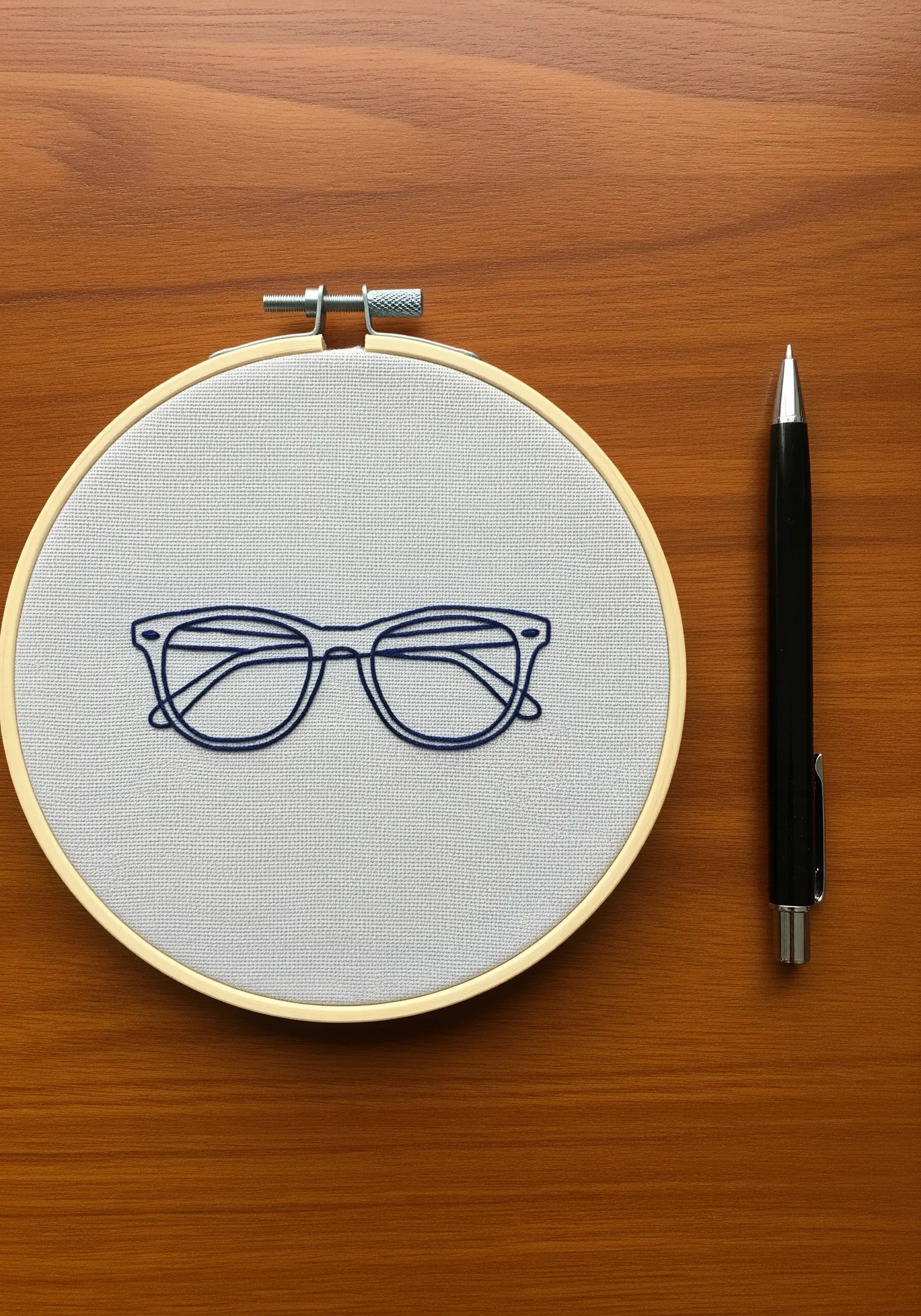 A precise outline of a pair of eyeglasses stitched in dark blue on gray fabric.