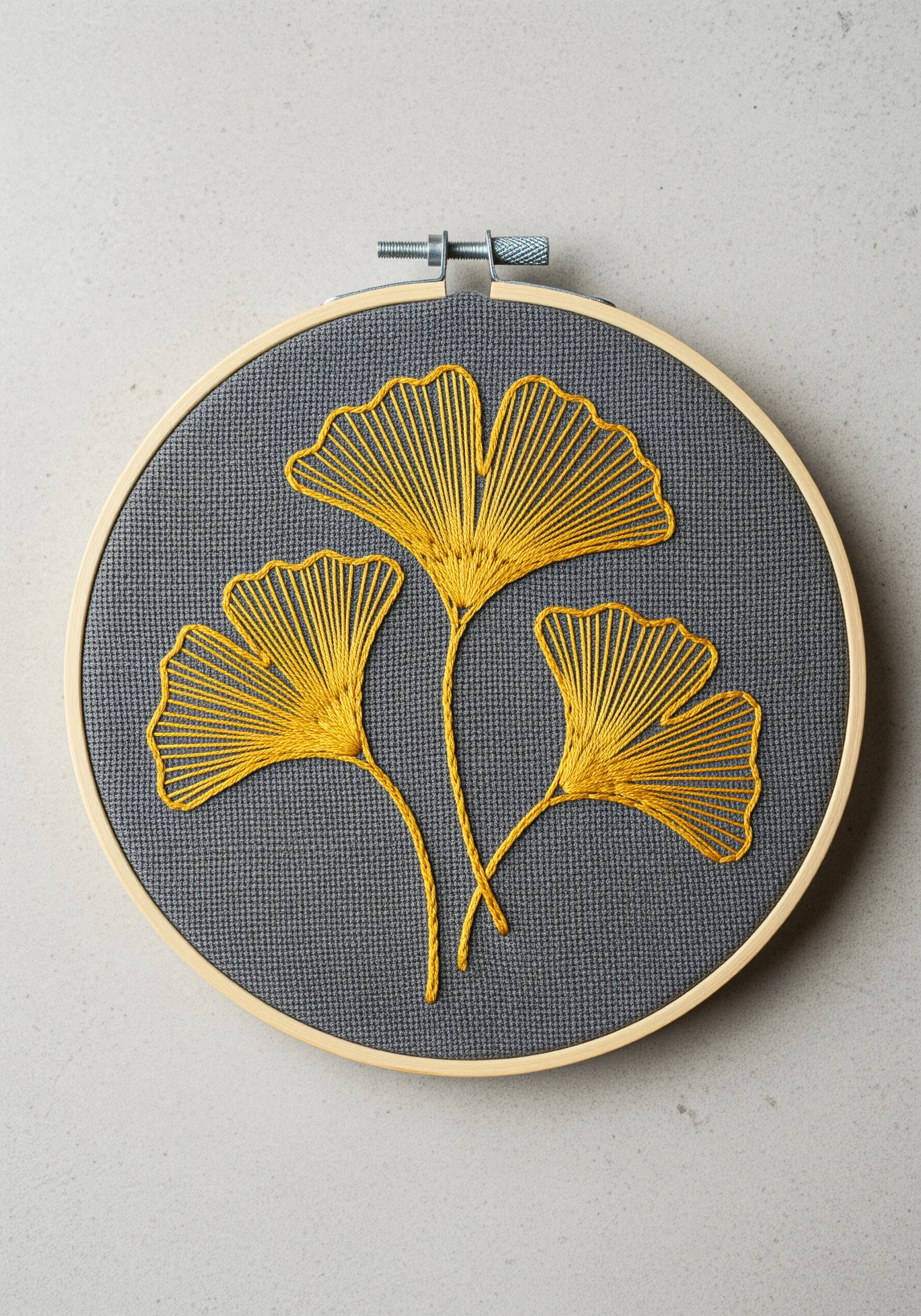 Three golden ginkgo leaves with radiating straight stitches embroidered on dark grey fabric.