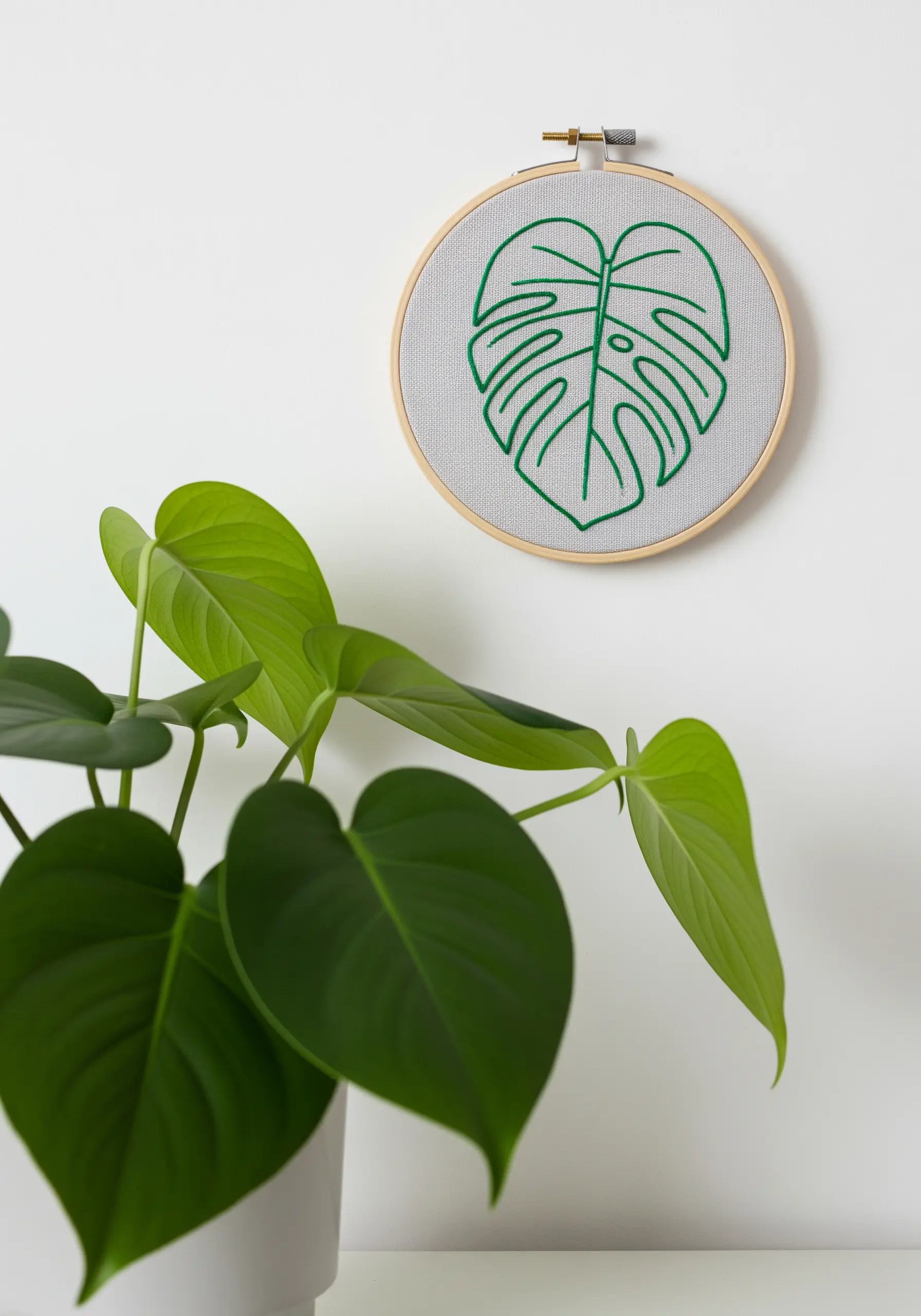 A line art embroidery of a Monstera leaf in bright green on a gray fabric.