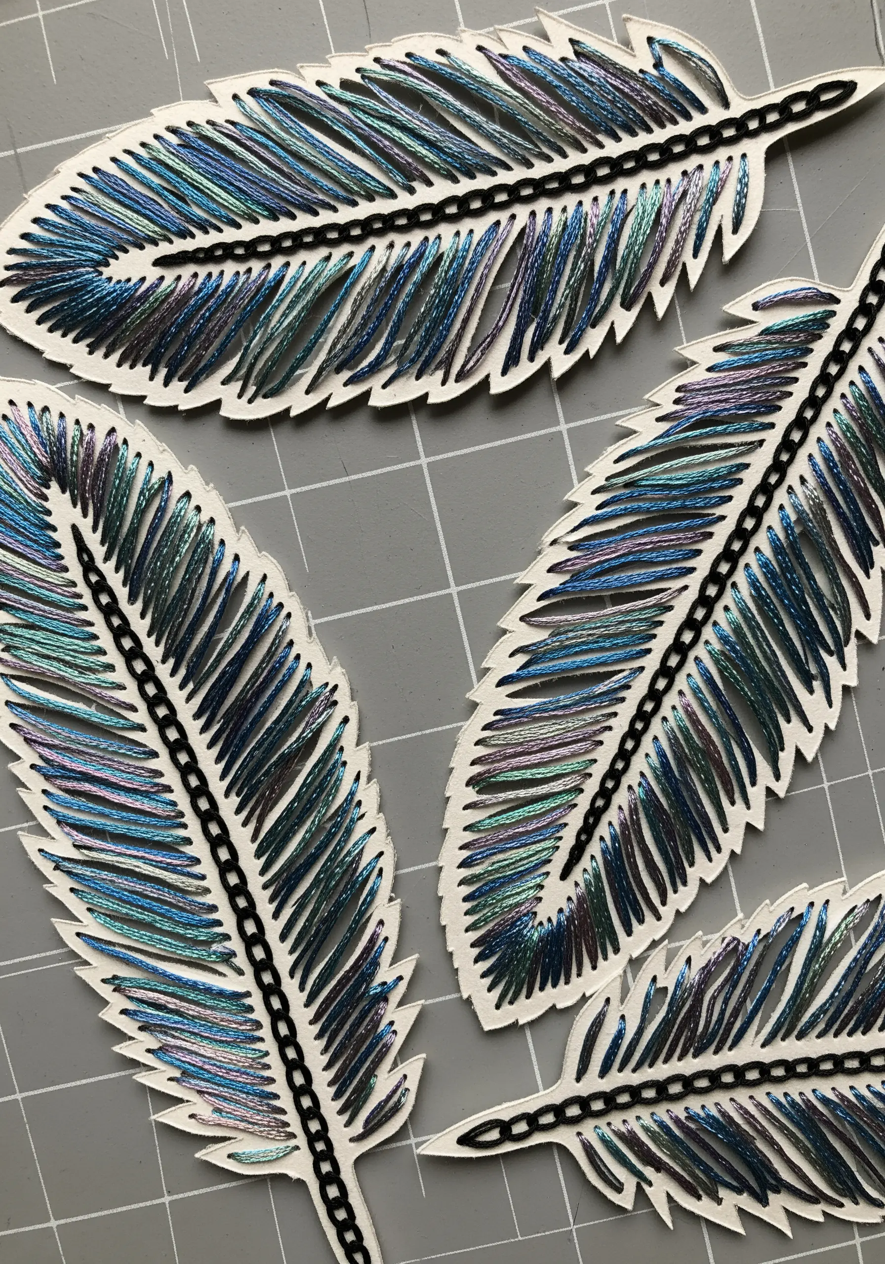Embroidery on cut-out paper feathers using iridescent variegated thread.