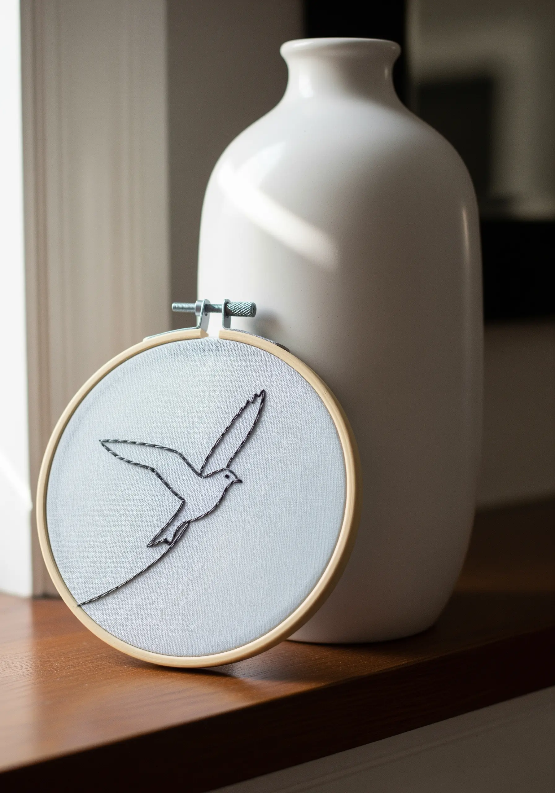 A simple line art drawing of a bird in flight, embroidered with black stem and back stitch.