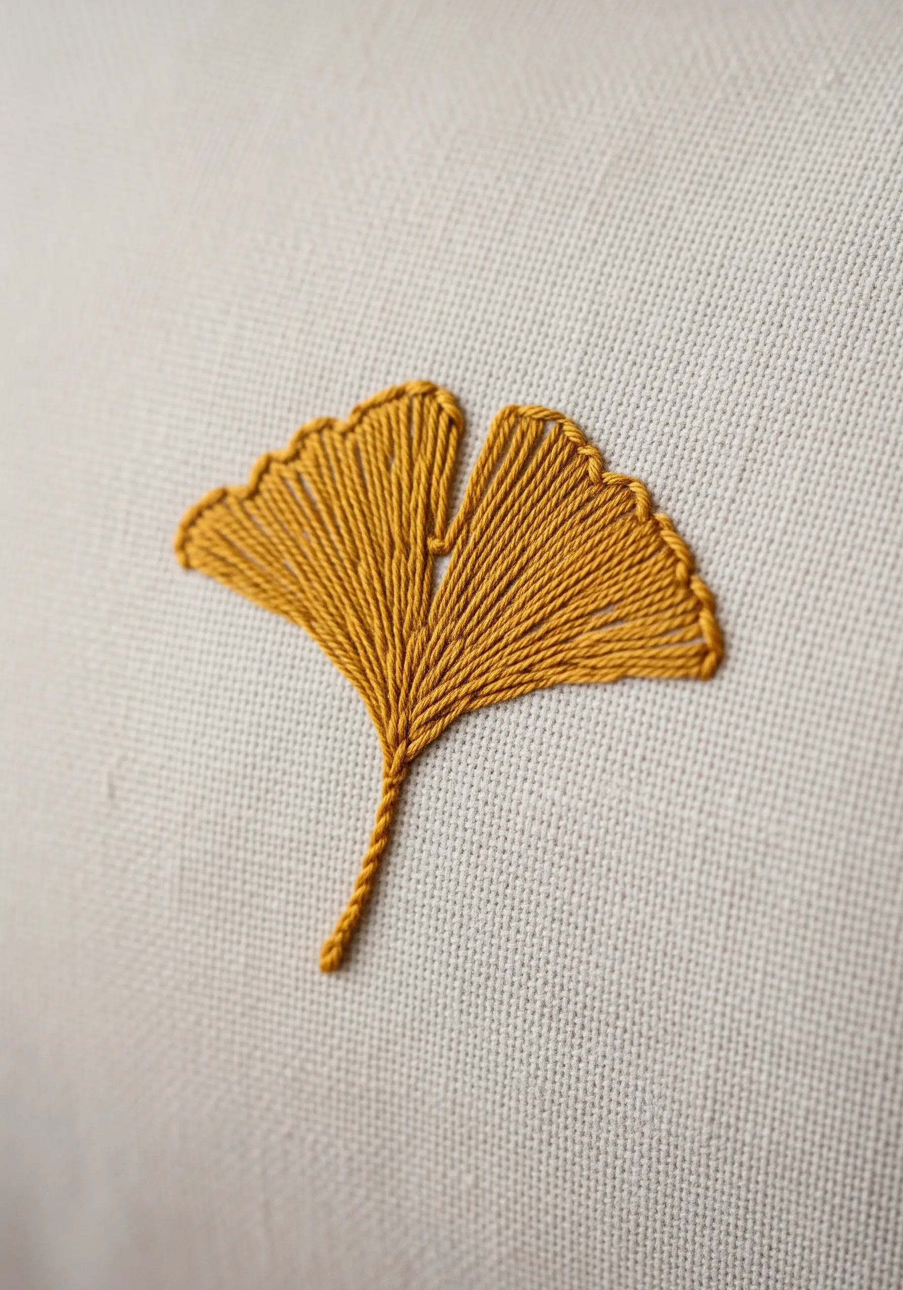 A single ginkgo leaf embroidered in mustard yellow thread on a light, textured pillowcase.