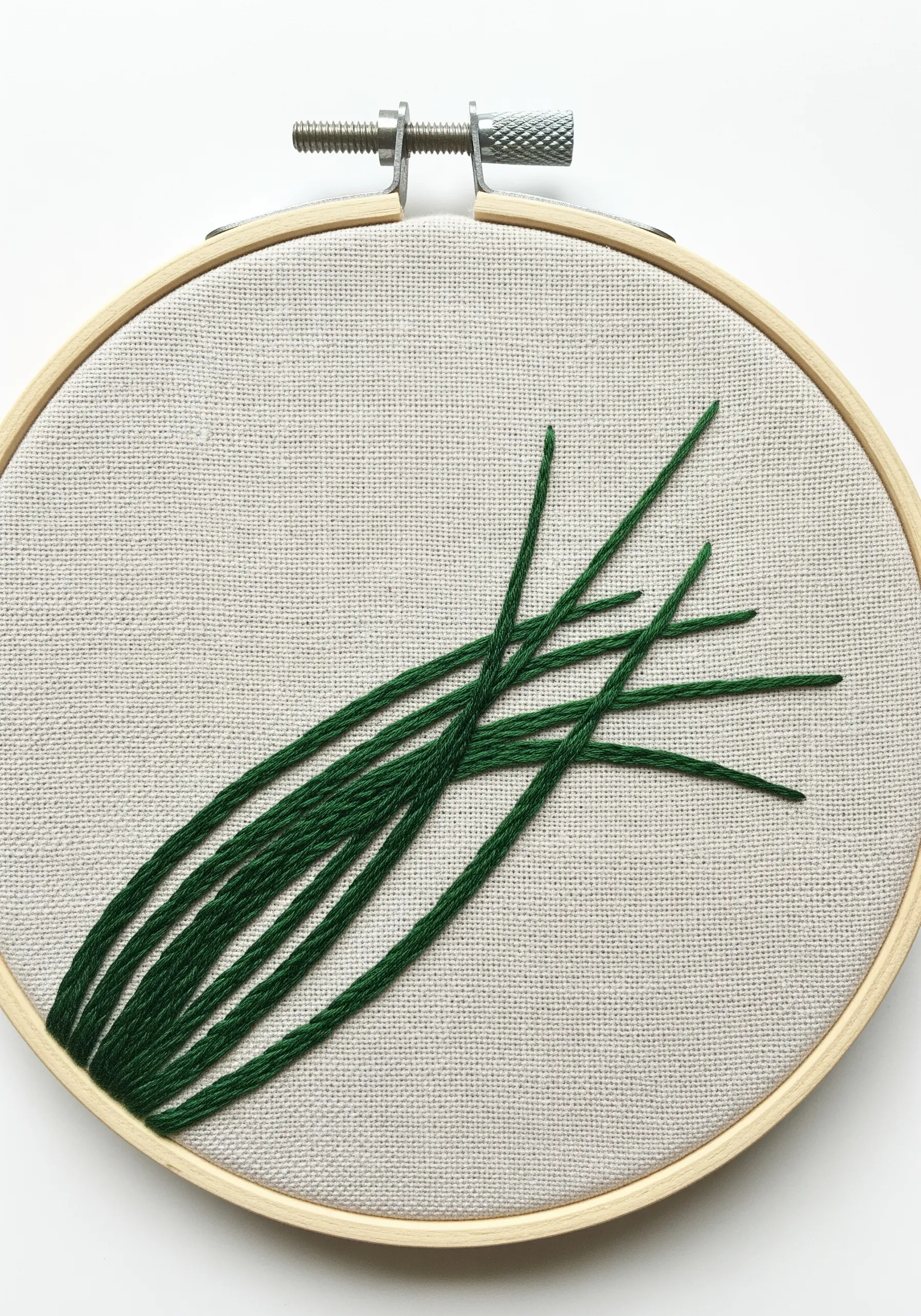 A bundle of chives embroidered with long, overlapping straight stitches in a deep green.
