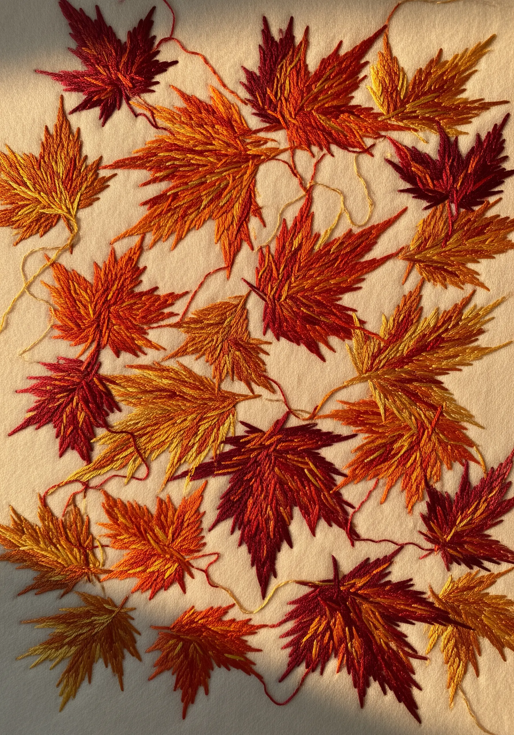Scattered autumn leaves embroidered with variegated threads in red, orange, and gold.