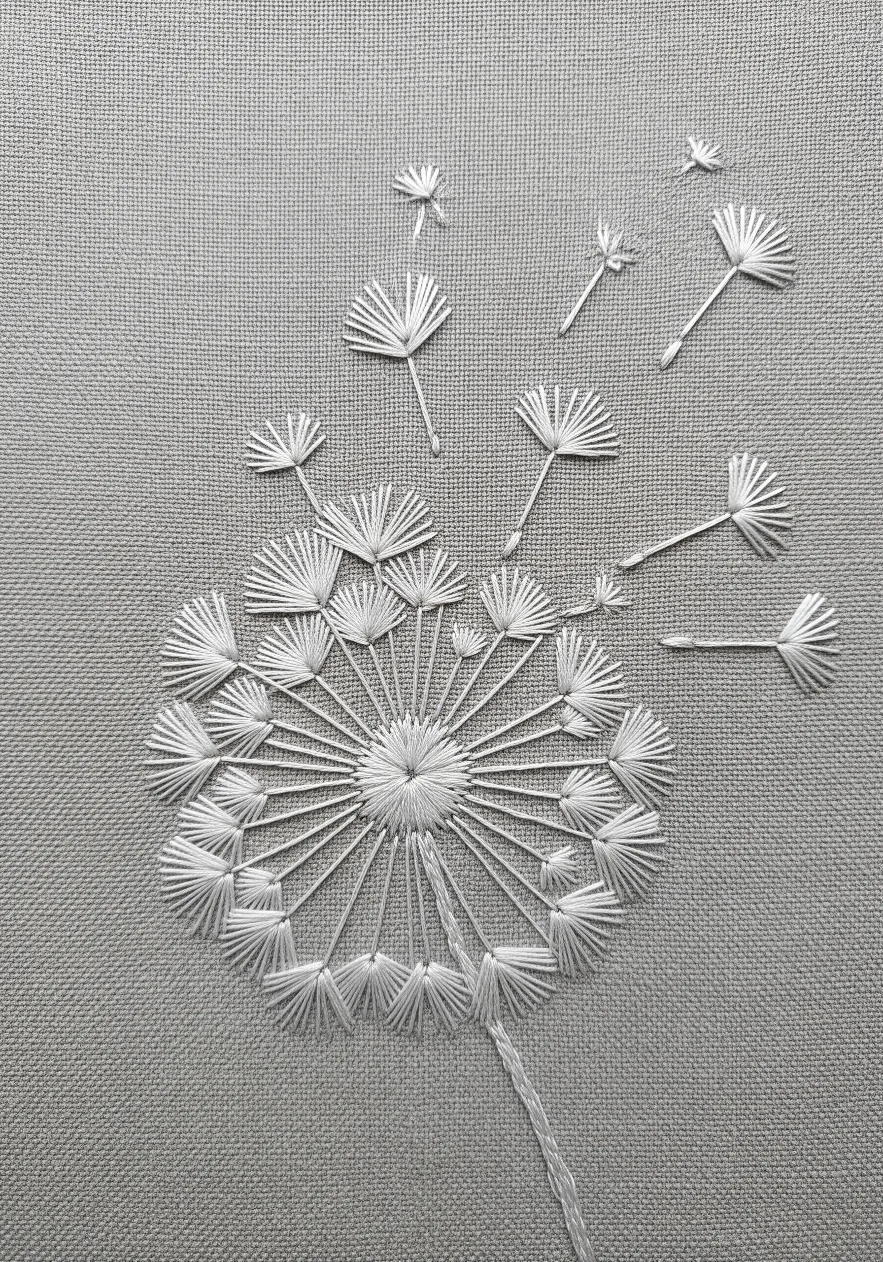 A dandelion head embroidered in white thread with seeds blowing away.