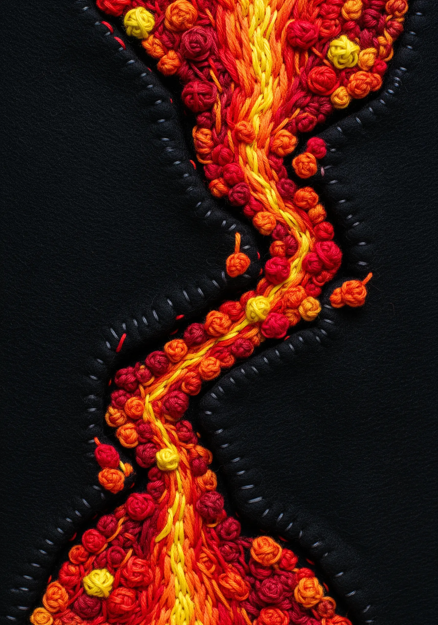 A river of red, orange, and yellow French knots flowing across black fabric.